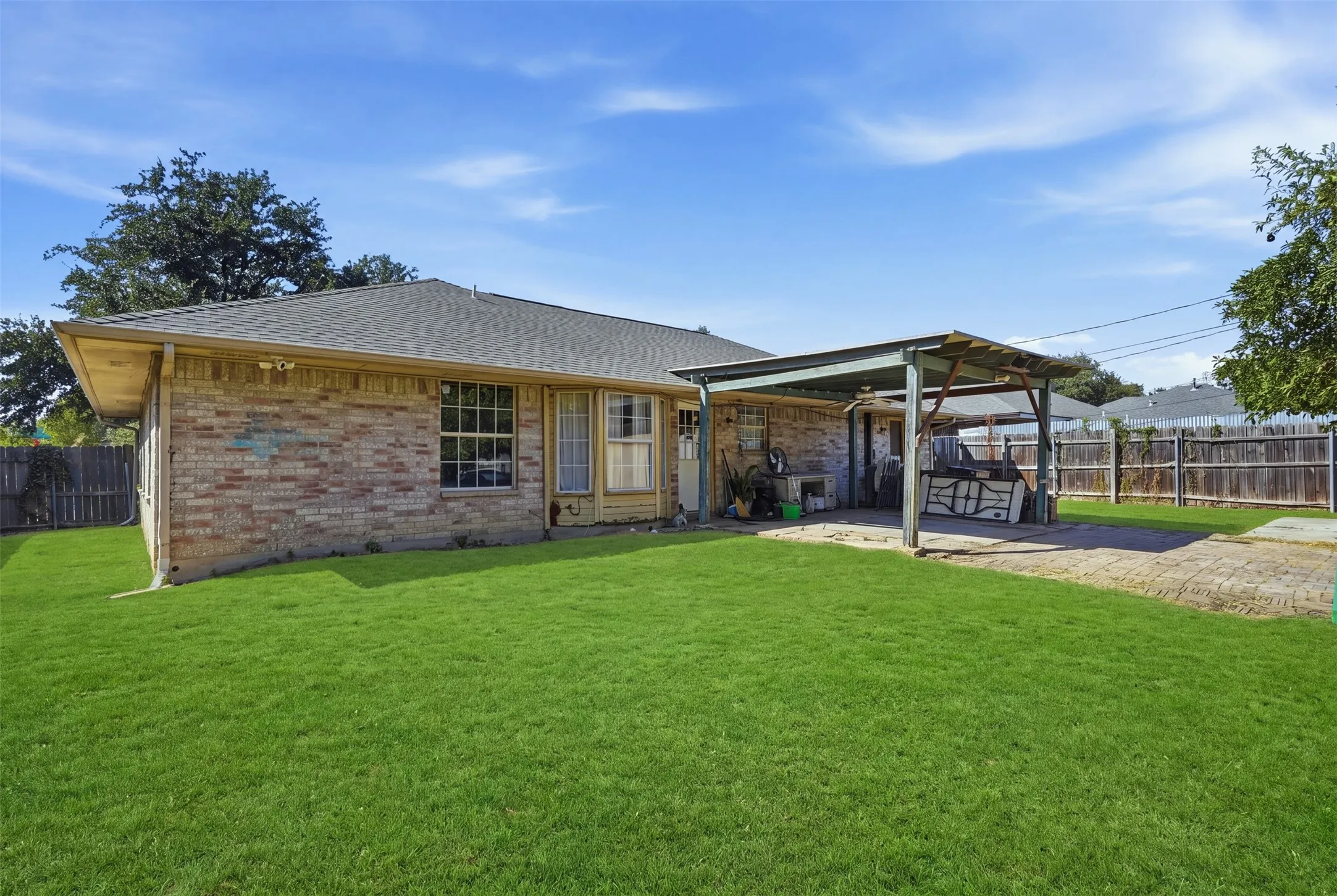 Expansive green lawn, brick exterior, covered patio structure, paved patio area, and wood fencing