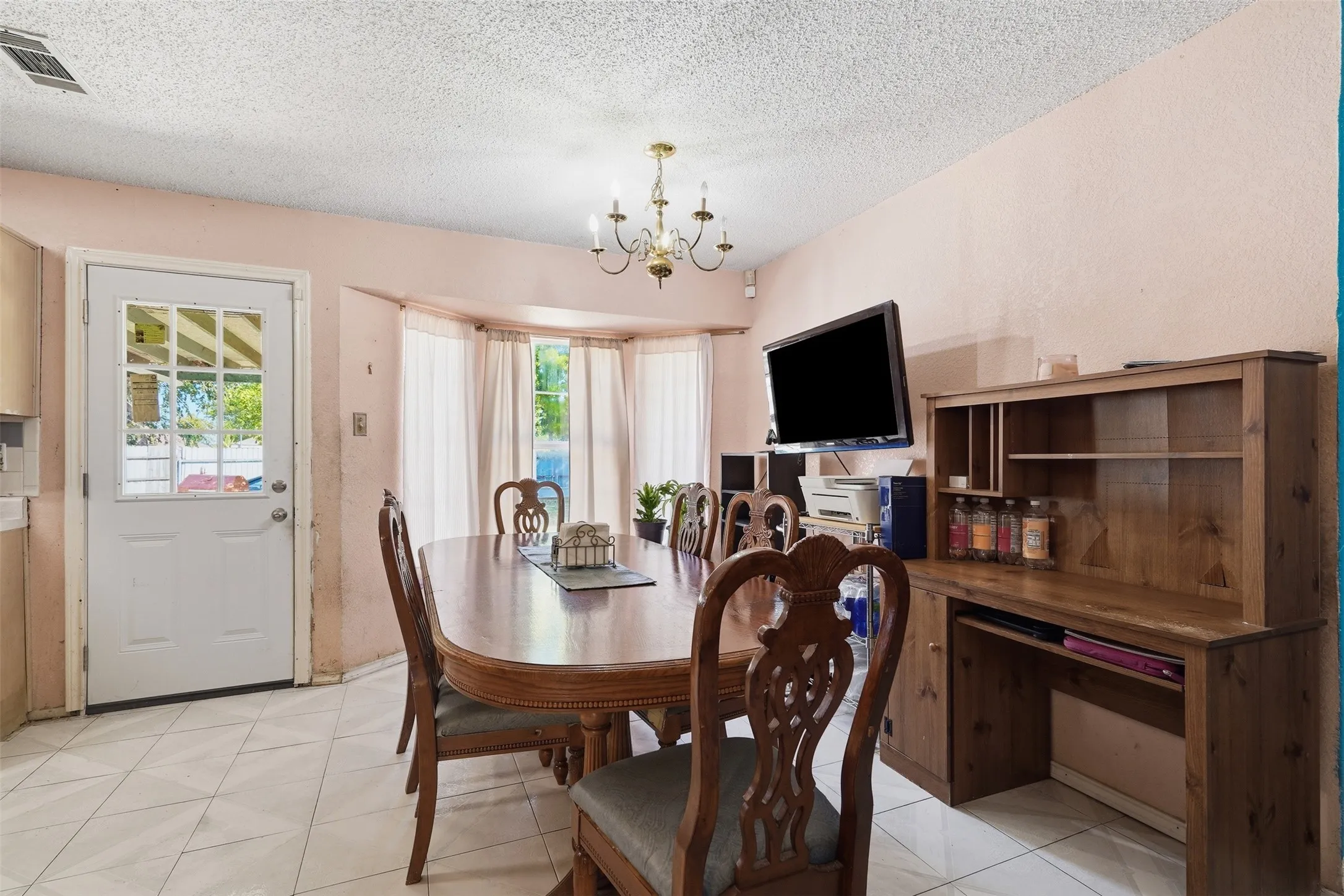 White tile flooring, bay window with drapes, glass-paneled exterior door, built-in wooden cabinetry, and overhead chandelier