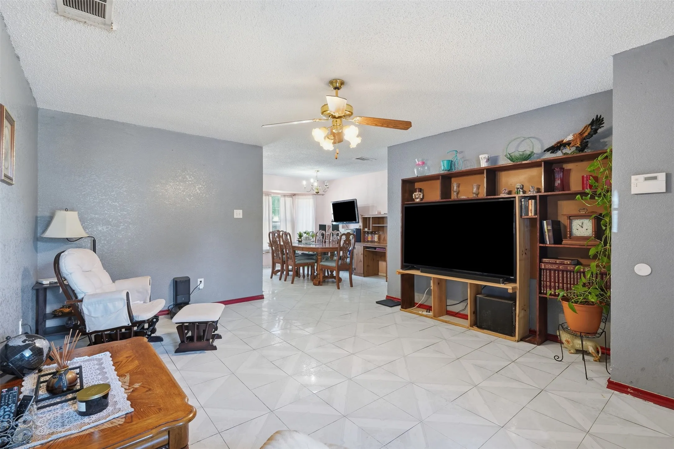 Spacious living area featuring patterned tile flooring, a ceiling fan with integrated lighting, and a built-in entertainment center with open shelving