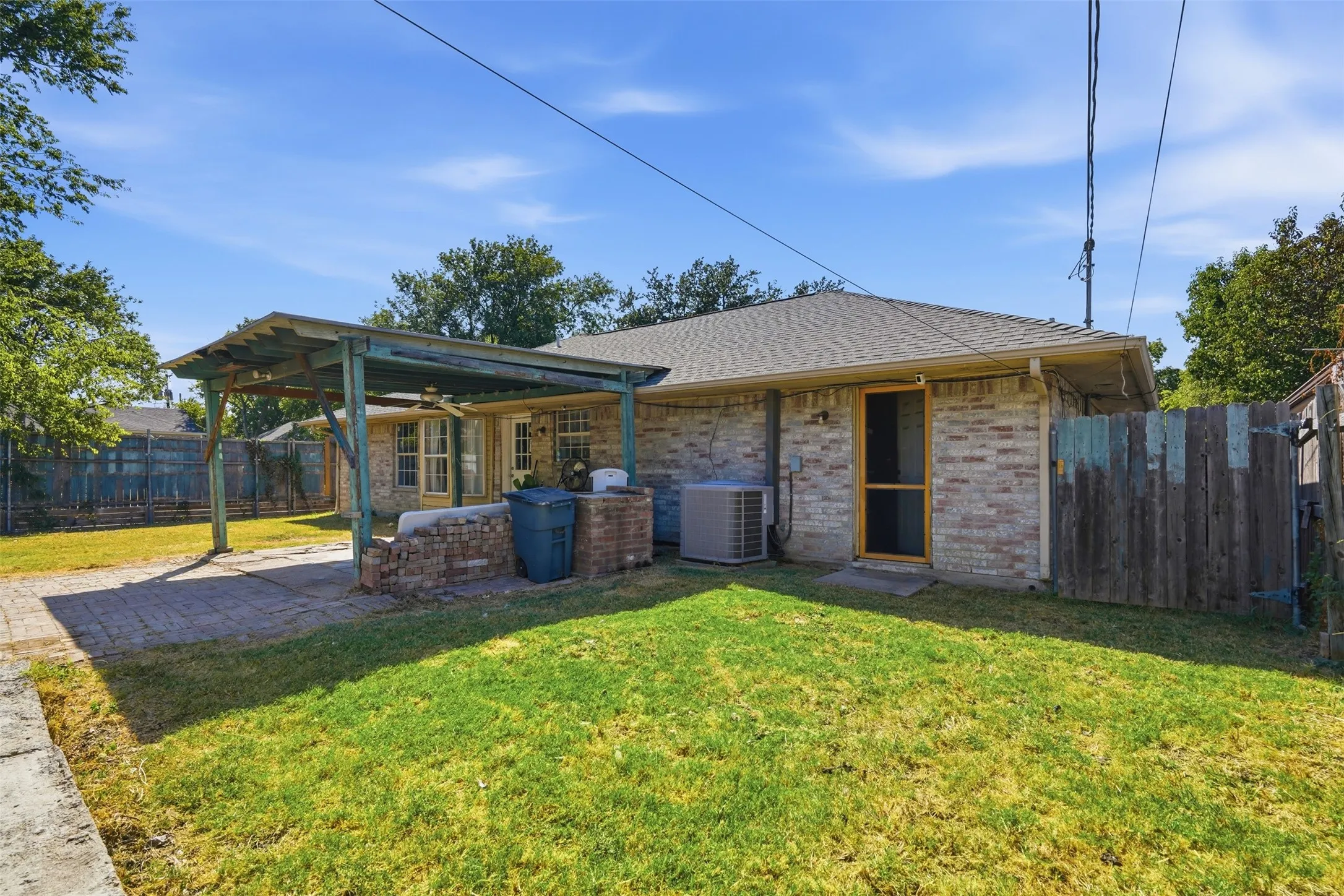 Brick exterior with a covered patio, paved patio surface, and a grassy backyard area