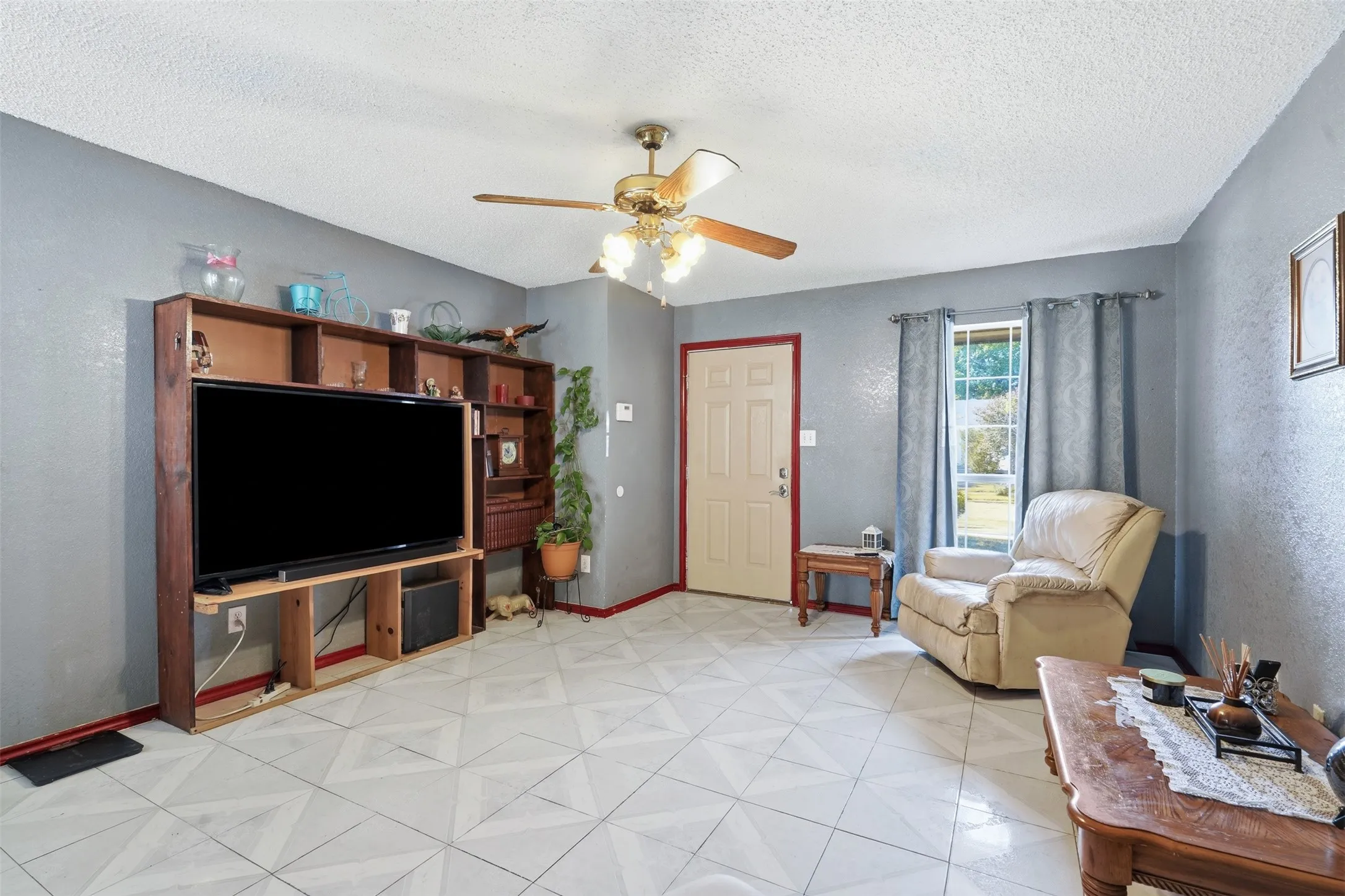 Living area featuring patterned tile flooring, a ceiling fan with integrated lighting, and a window with exterior views