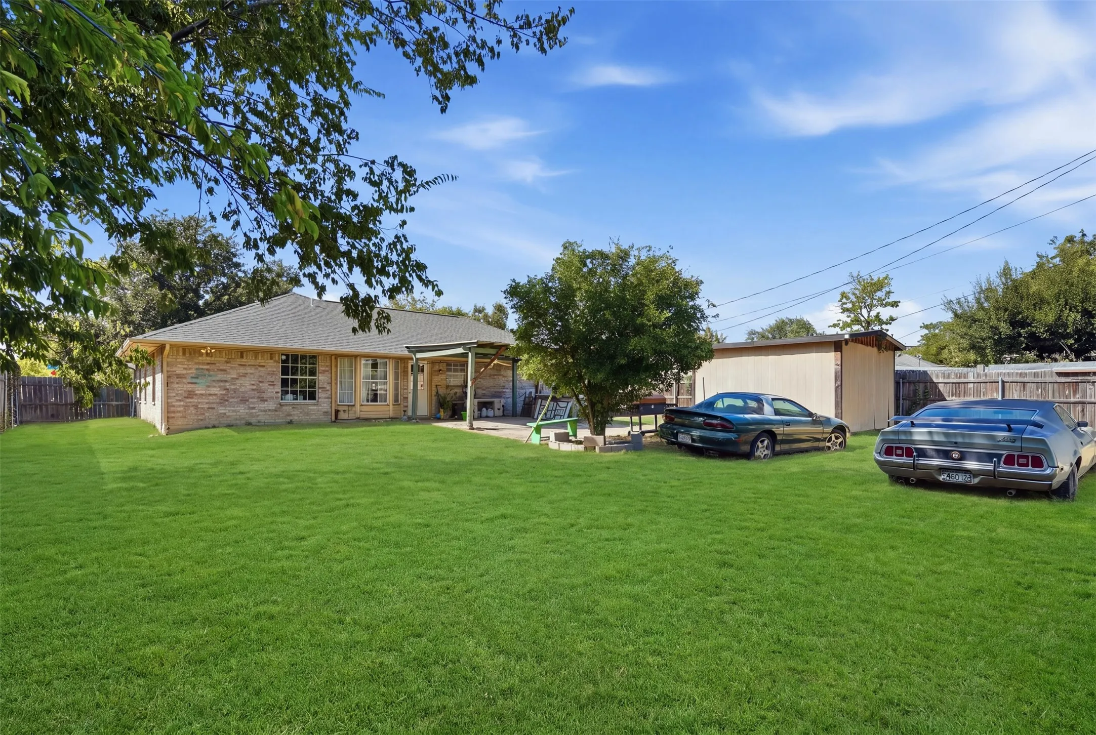 Expansive backyard featuring a manicured lawn, brick exterior, covered patio, and detached storage shed