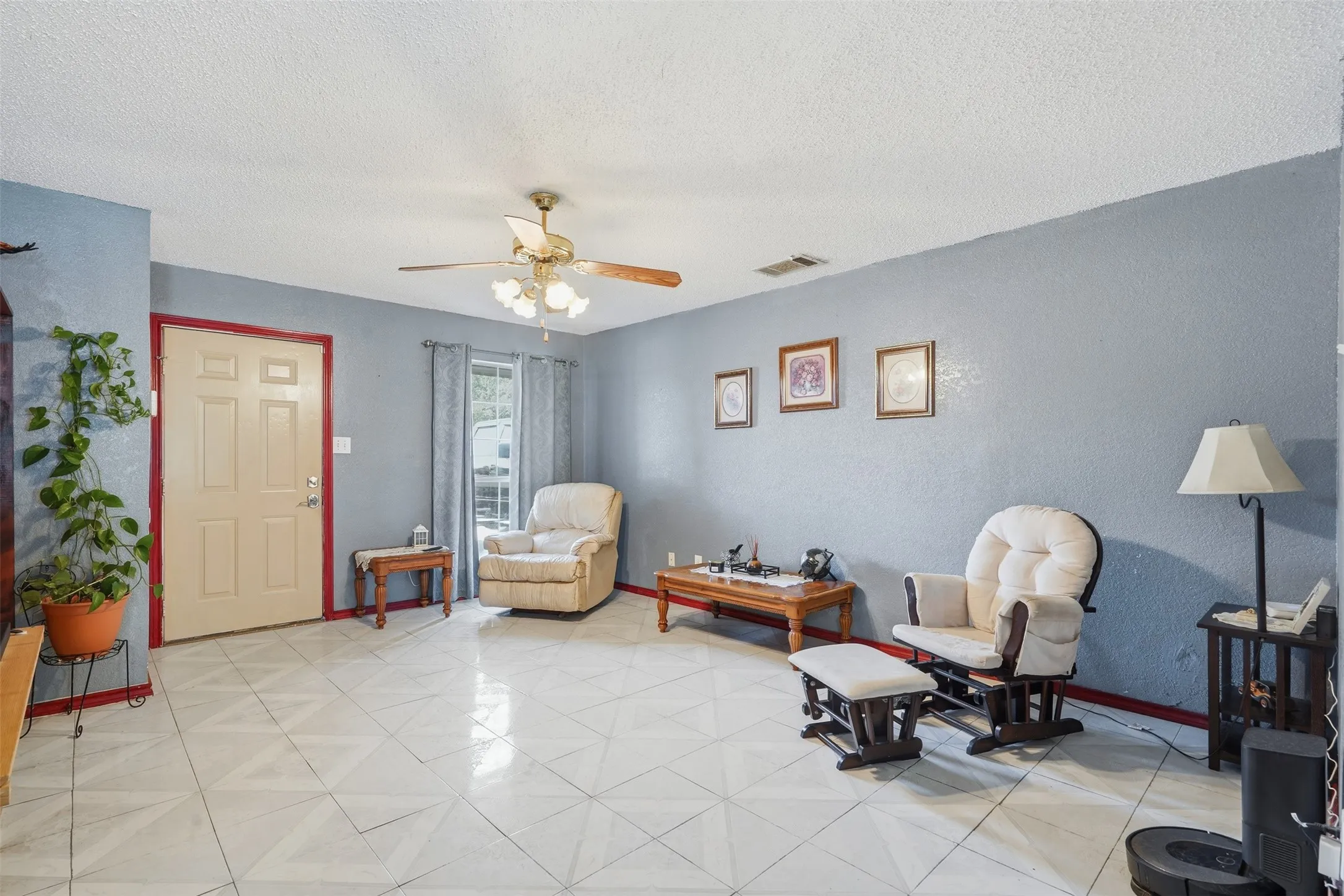 Patterned tile flooring, ceiling fan with integrated lighting, paneled entry door, and a window with curtain rods