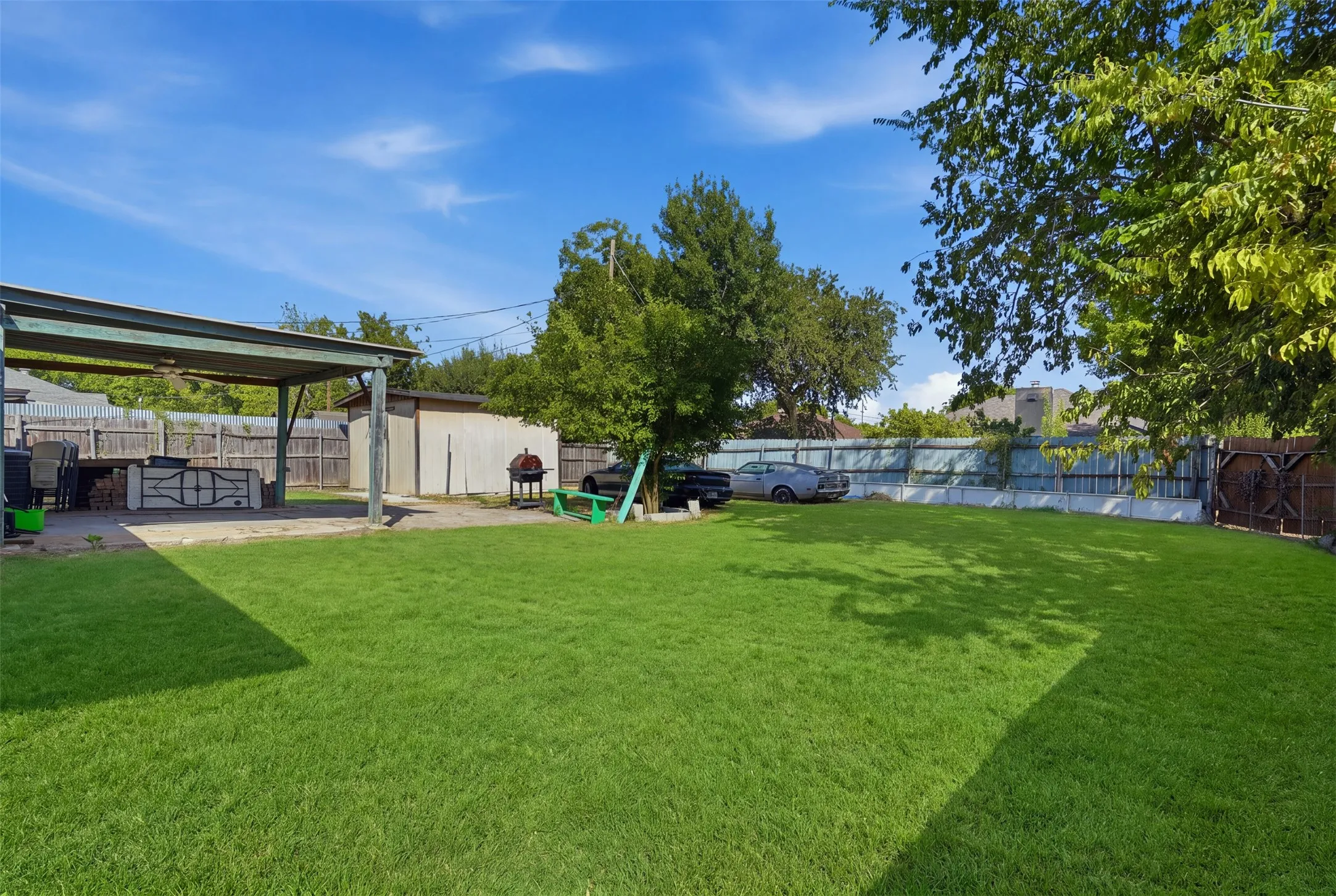 Expansive backyard featuring a manicured lawn, covered patio, storage shed, and mature trees
