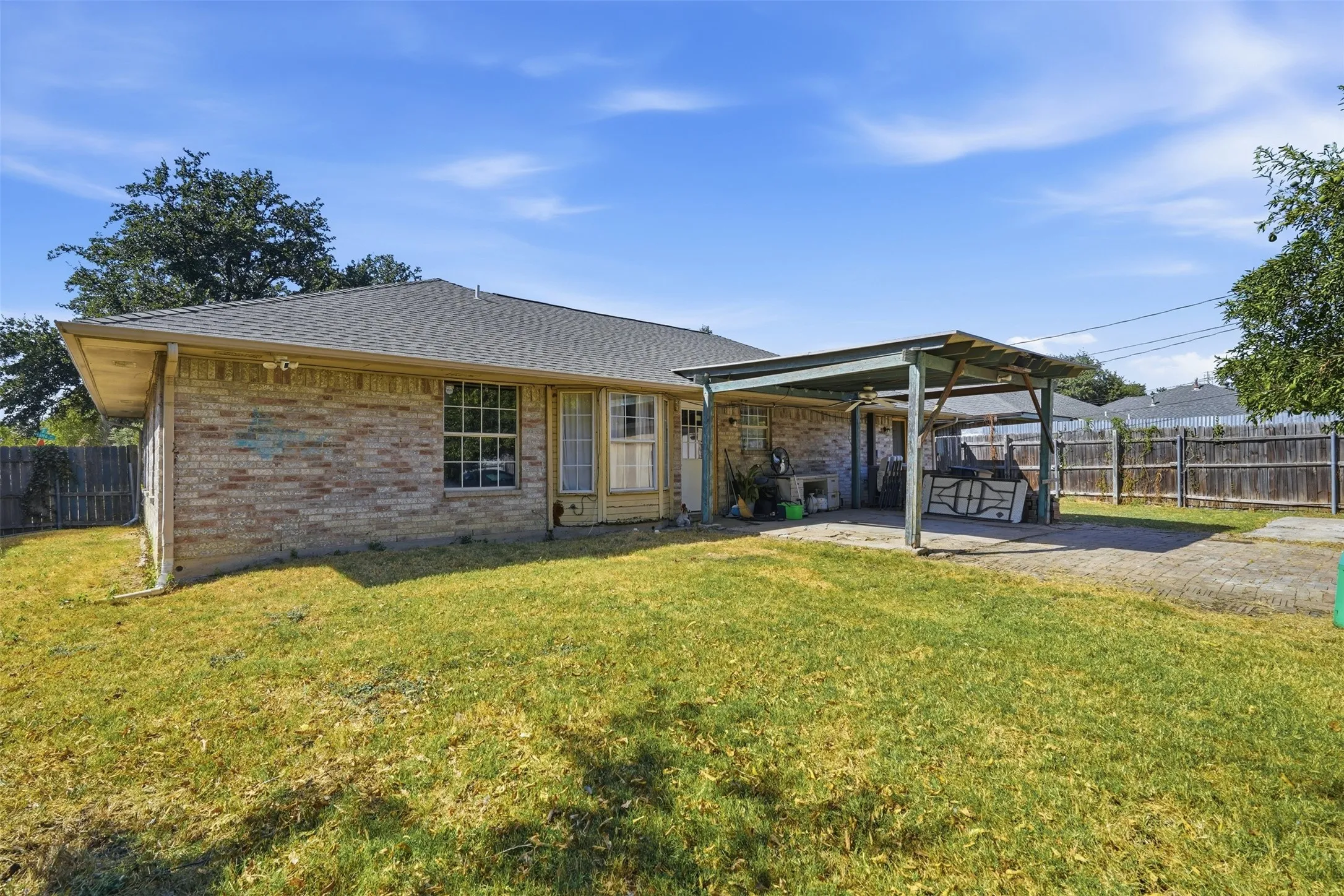 Brick exterior with a shingle roof, featuring a covered patio with a metal frame, and a paved area