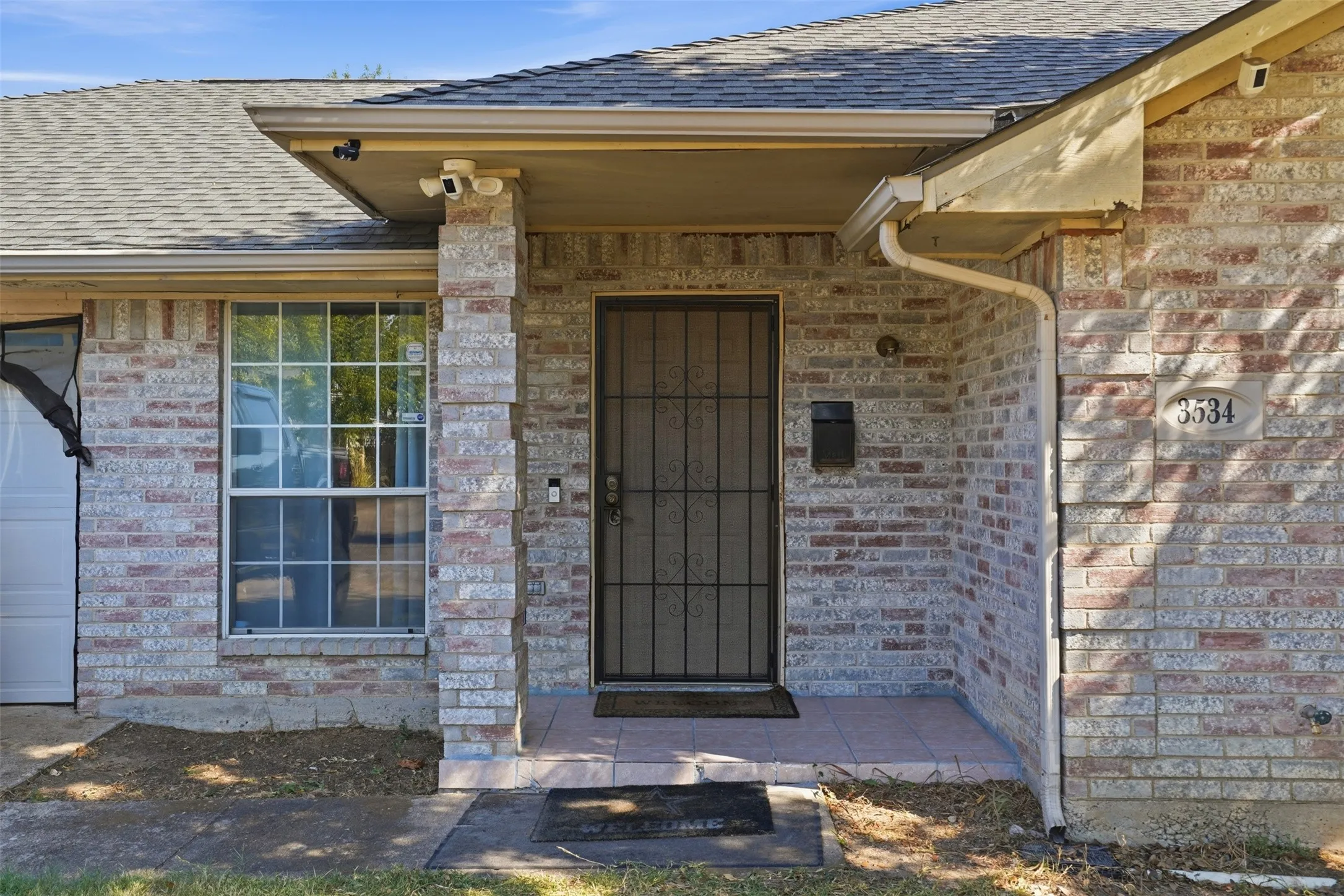 Brick exterior featuring a covered entry, security door, and a single window with grilles