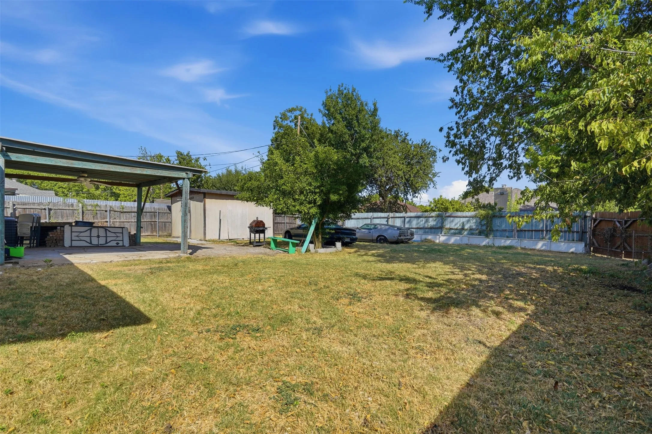 Expansive backyard featuring a large open lawn, a covered patio structure, and a detached shed