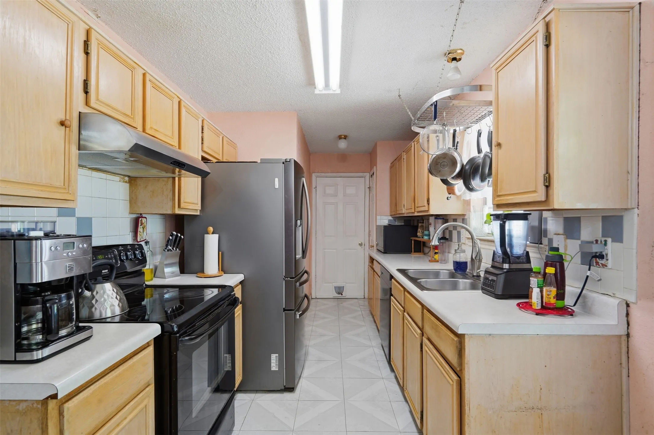 Galley kitchen featuring wood cabinetry, white countertops, tile flooring, and a stainless steel refrigerator