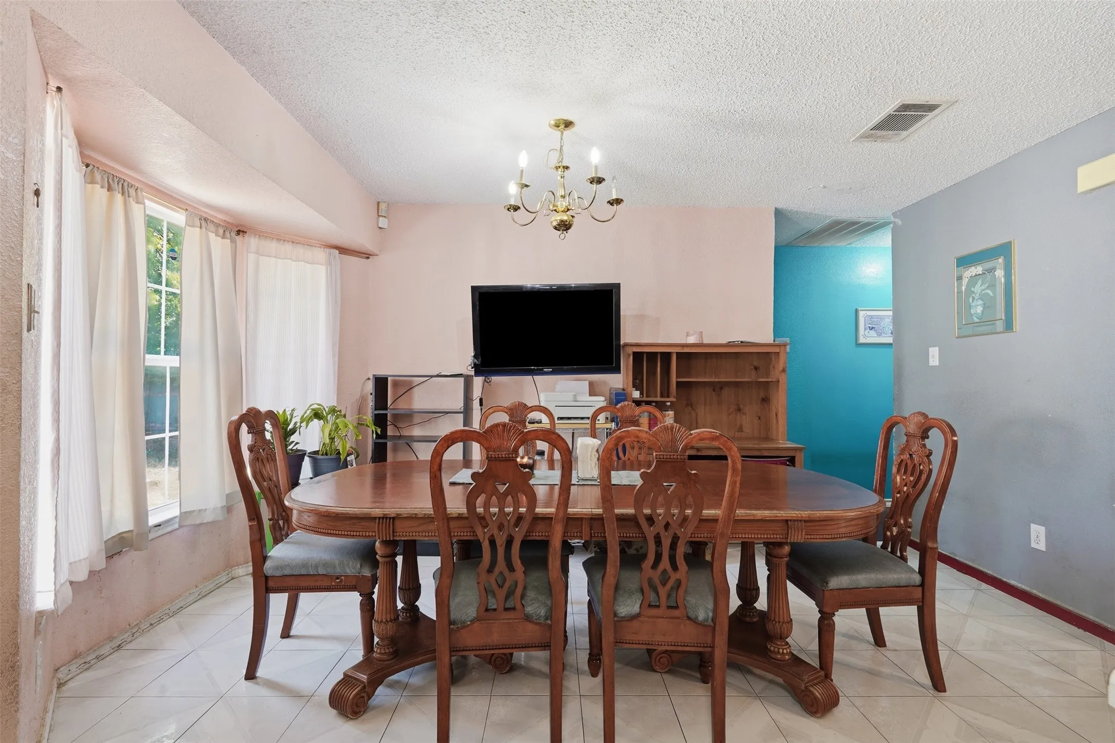 Elegant dining room featuring a round wood pedestal table, ornate carved-wood chairs with upholstered seats, tile flooring, and a brass chandelier