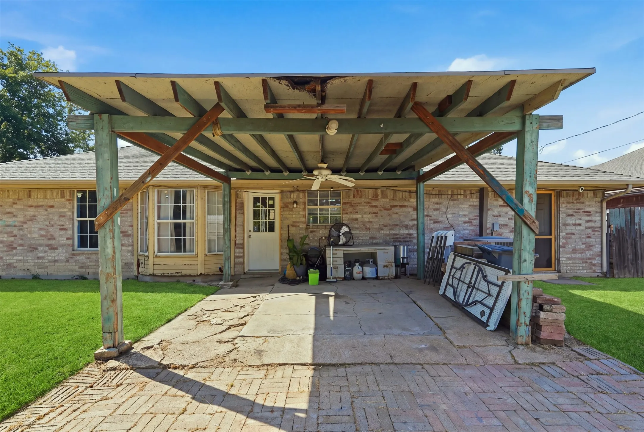 Covered patio with exposed wood beams, brick paver flooring, and concrete slab