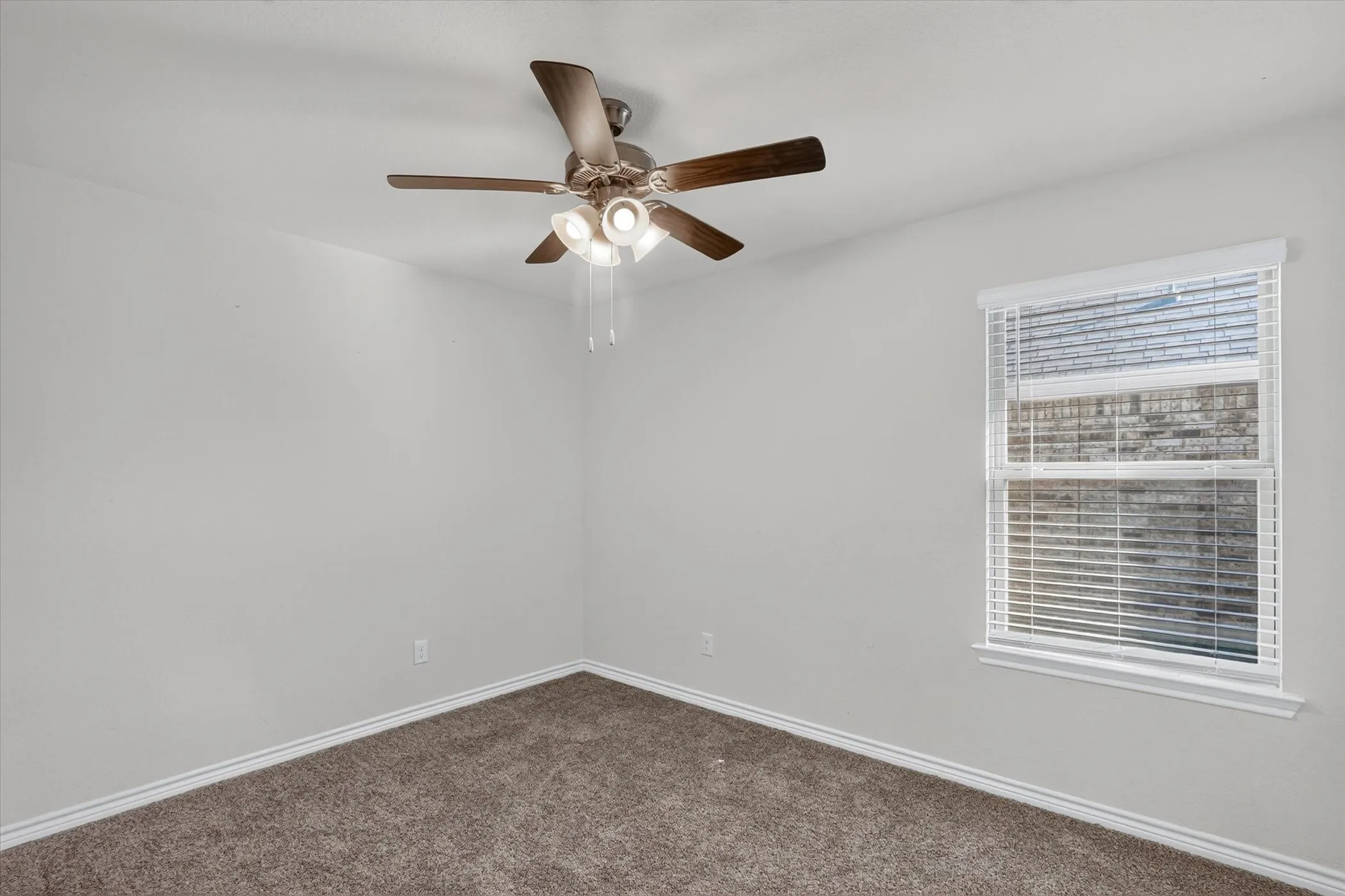 Light gray painted walls, brown carpet flooring, and a ceiling fan with integrated lighting