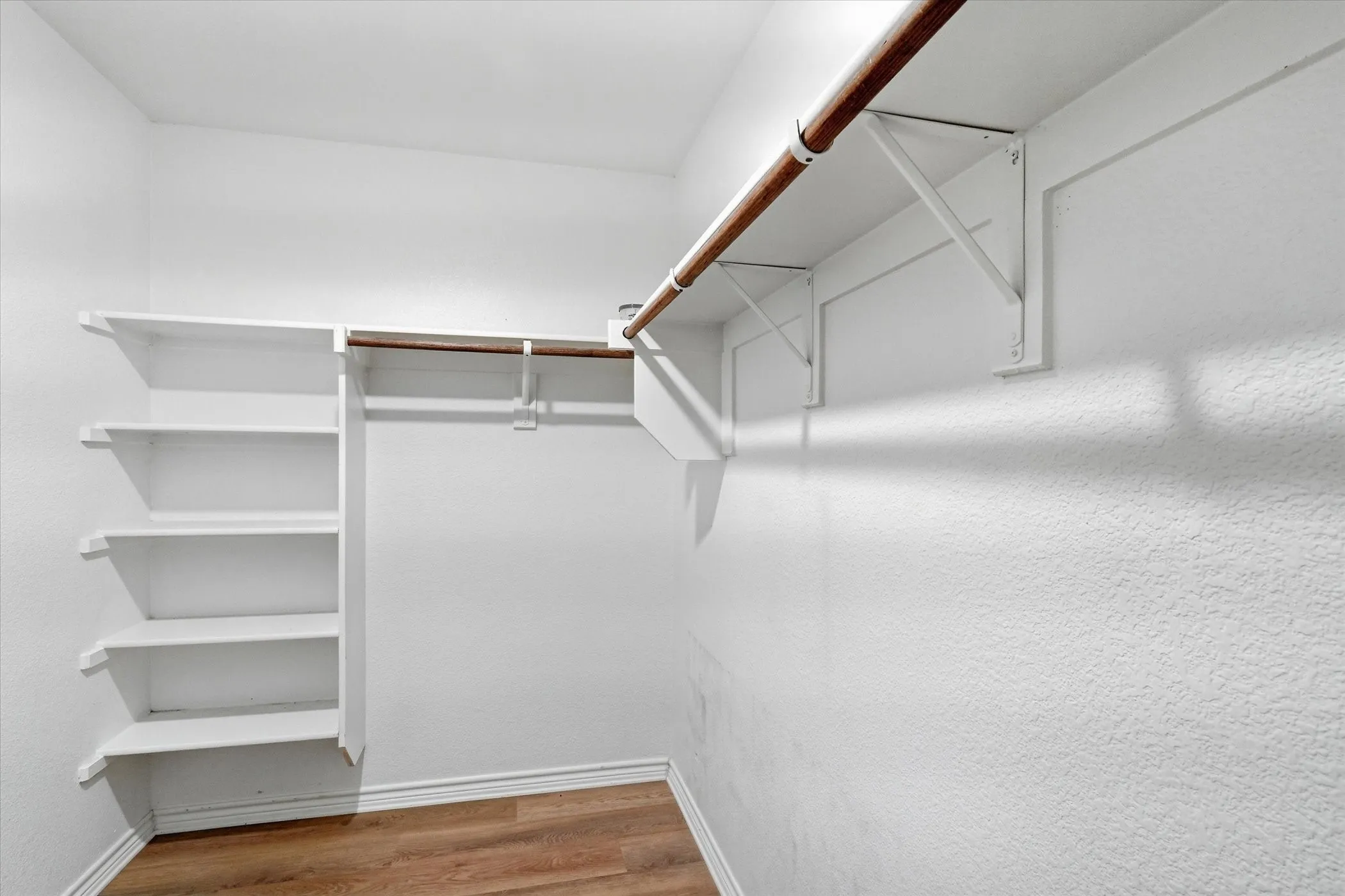 Walk-in closet featuring wood-finish flooring, multiple shelving units, and a clothes hanging rod
