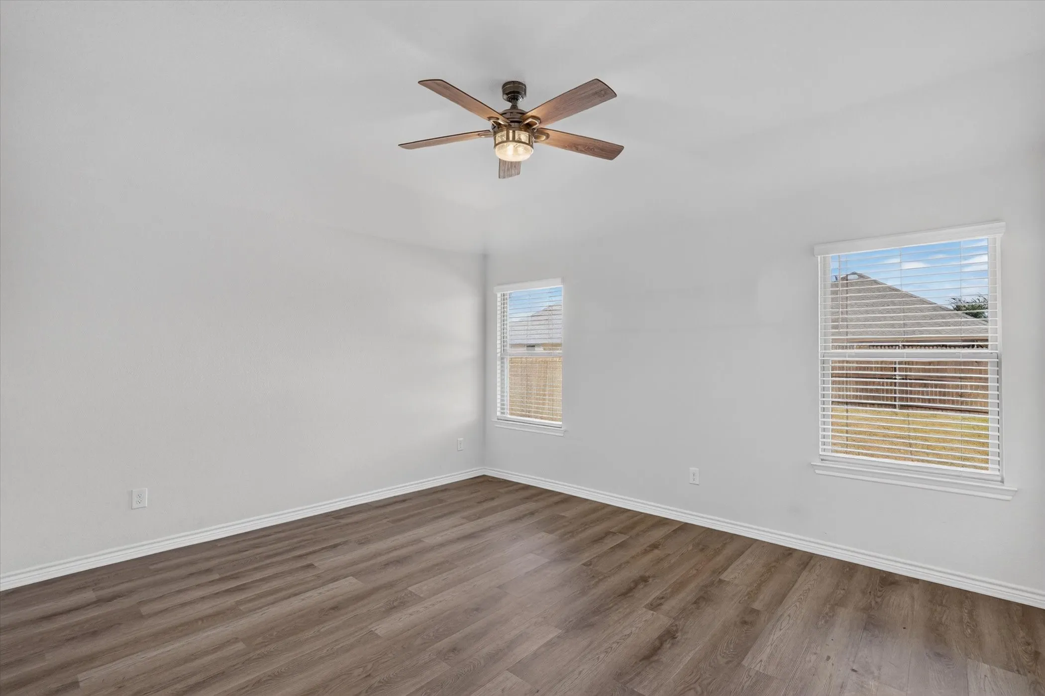 Vaulted ceiling with a ceiling fan, two windows with blinds, and wood-finish flooring