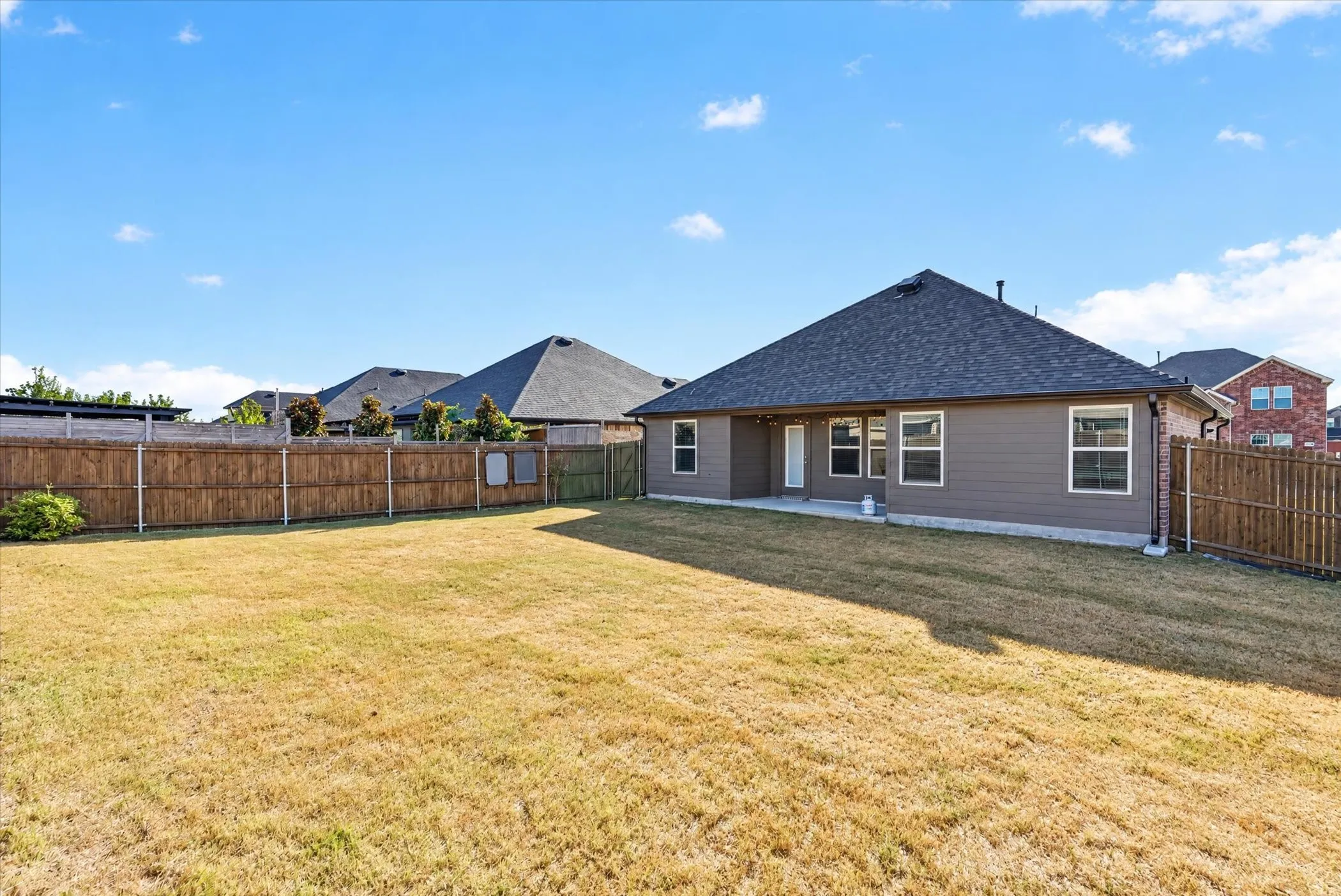 Expansive backyard featuring a wood fence, concrete patio, and a shingled roofline