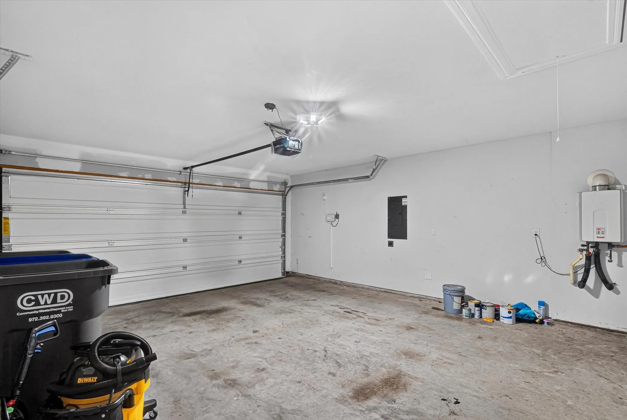 Garage featuring a roll-up door, automatic opener, concrete flooring, and a wall-mounted tankless water heater