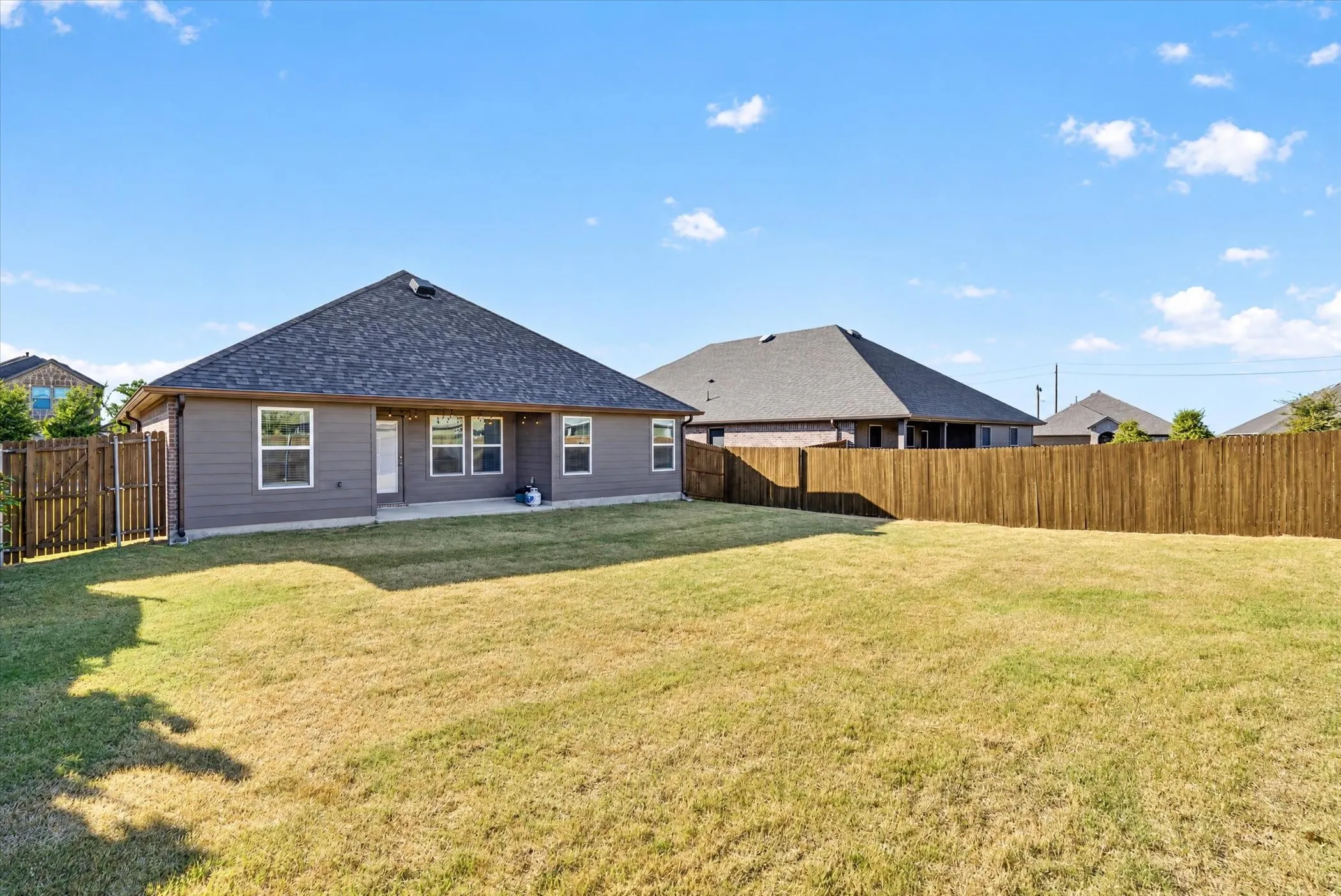 Expansive backyard featuring a privacy fence, a concrete patio, and a shingled roof