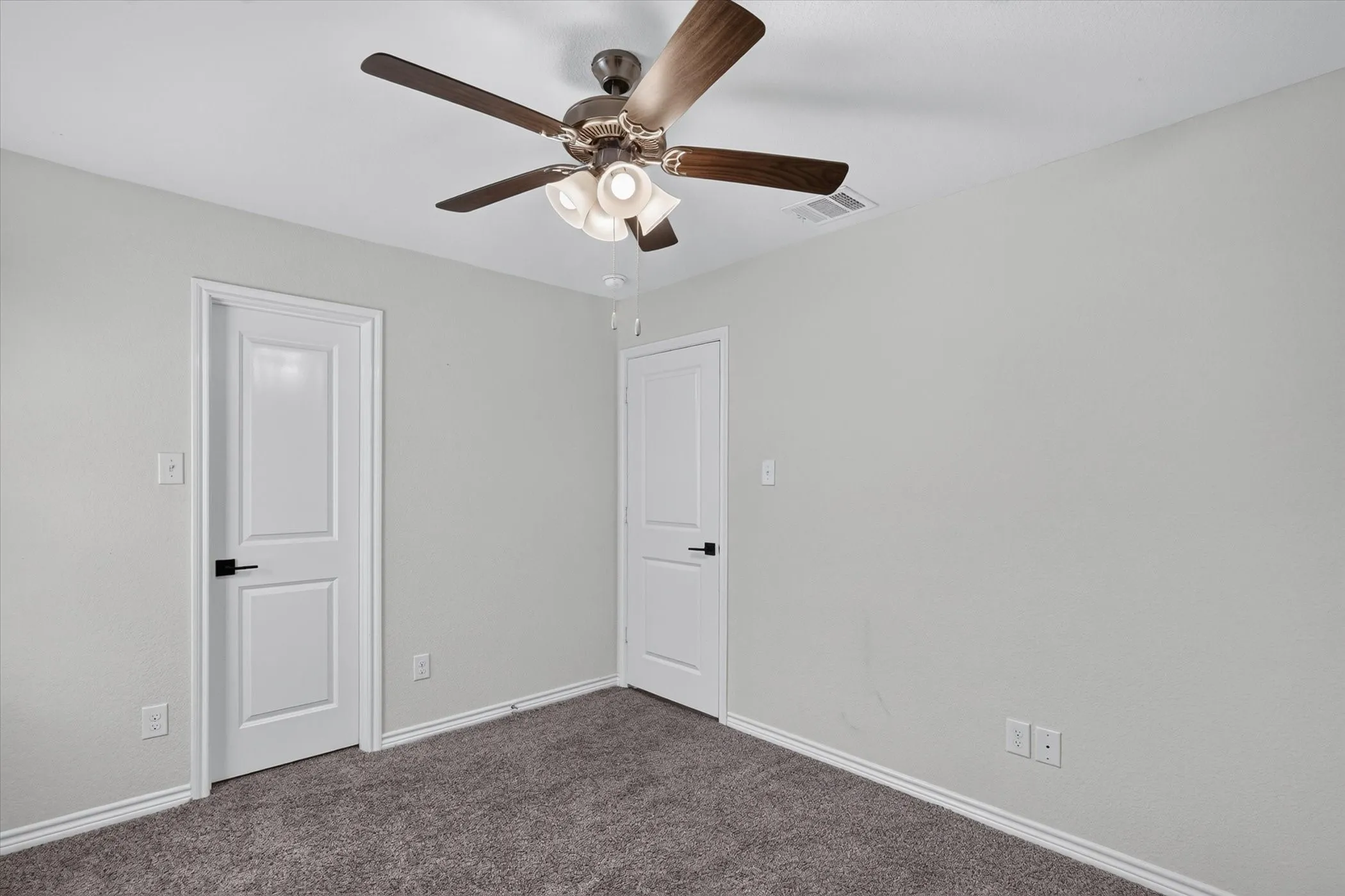 Ceiling fan with light kit, textured gray walls, two paneled doors with black hardware, and dark gray carpeting