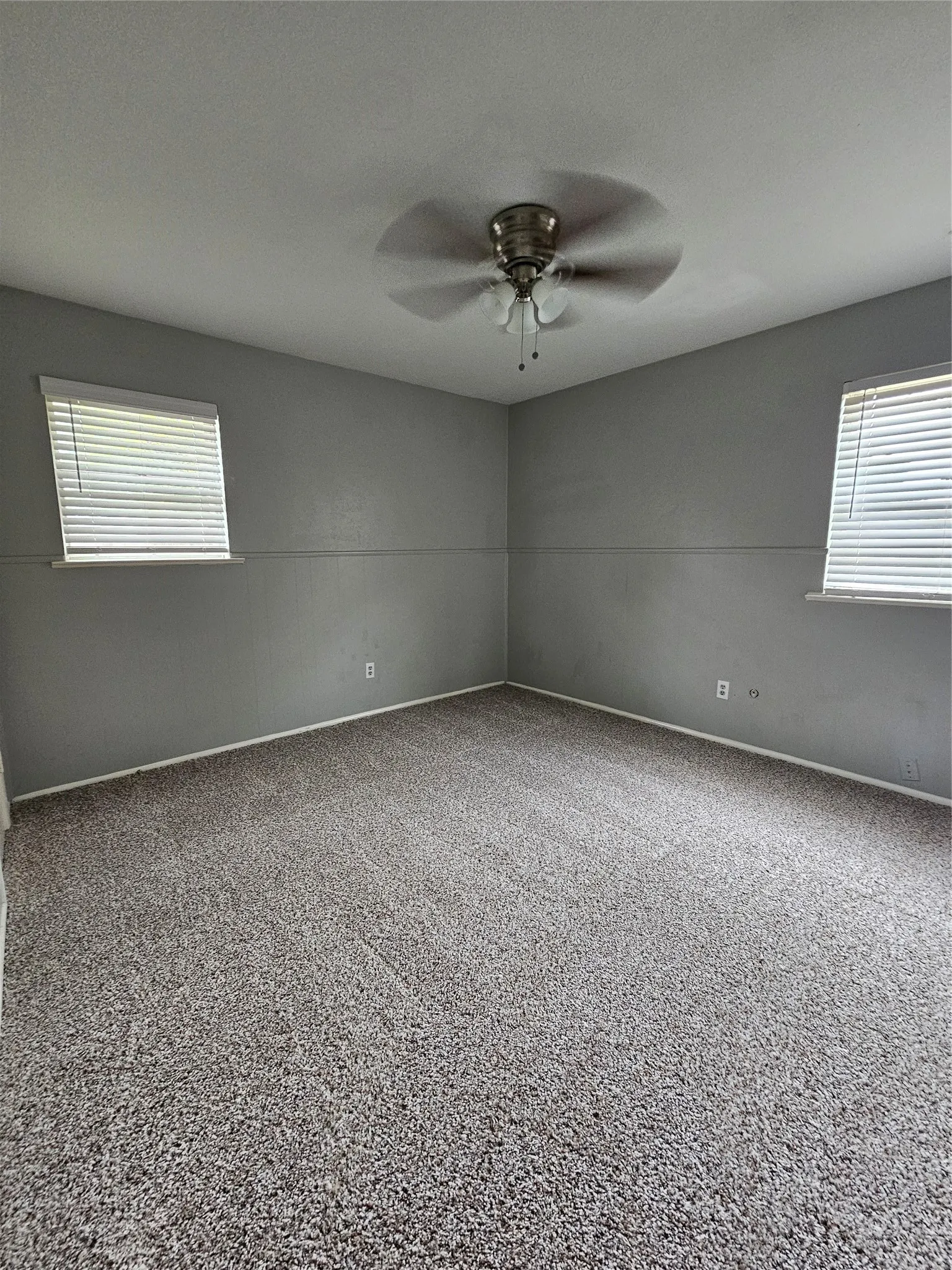 Wall-to-wall carpeting with light-toned walls, two windows with blinds, and a ceiling fan with integrated lighting