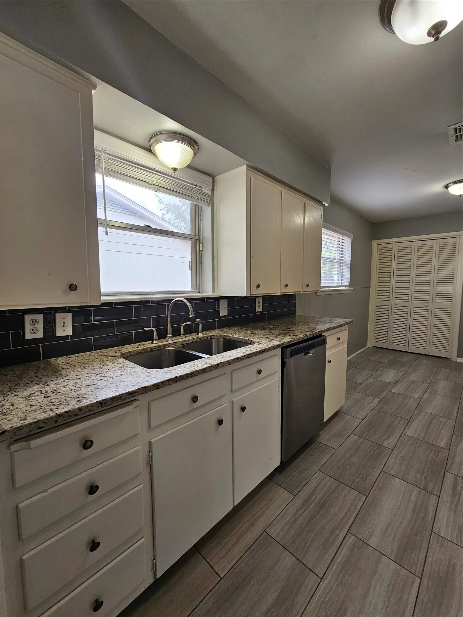 White cabinetry with dark hardware, stone-finish countertops, subway tile backsplash, and stainless steel sink