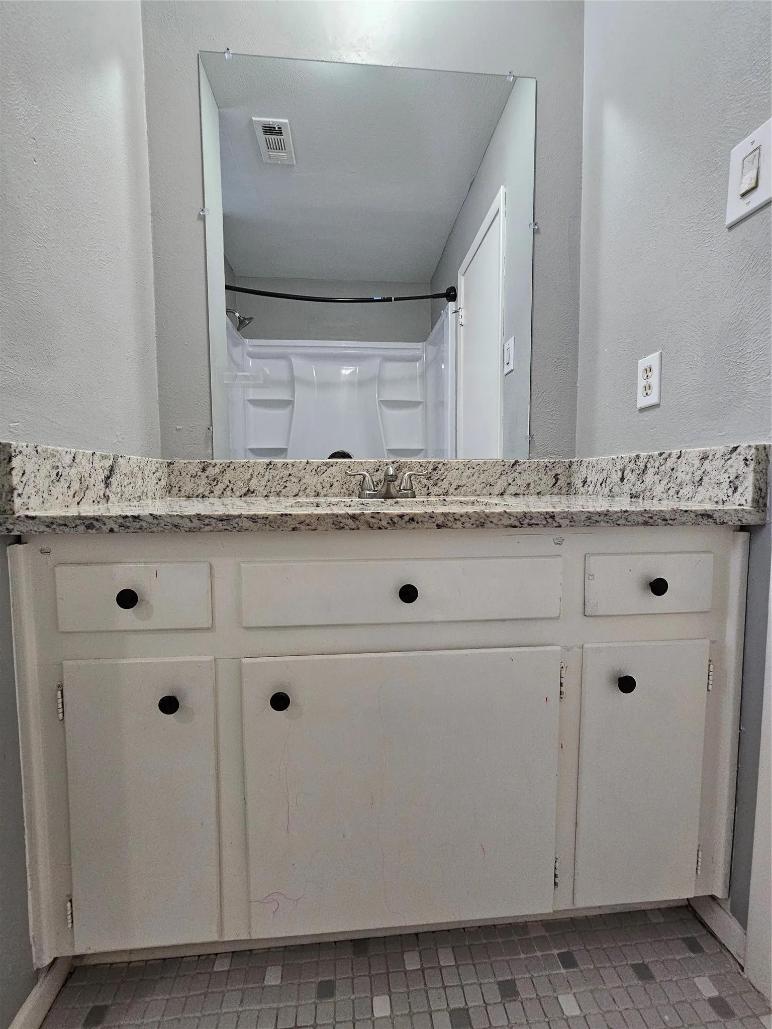 Vanity with a speckled countertop, white cabinetry, and black hardware
