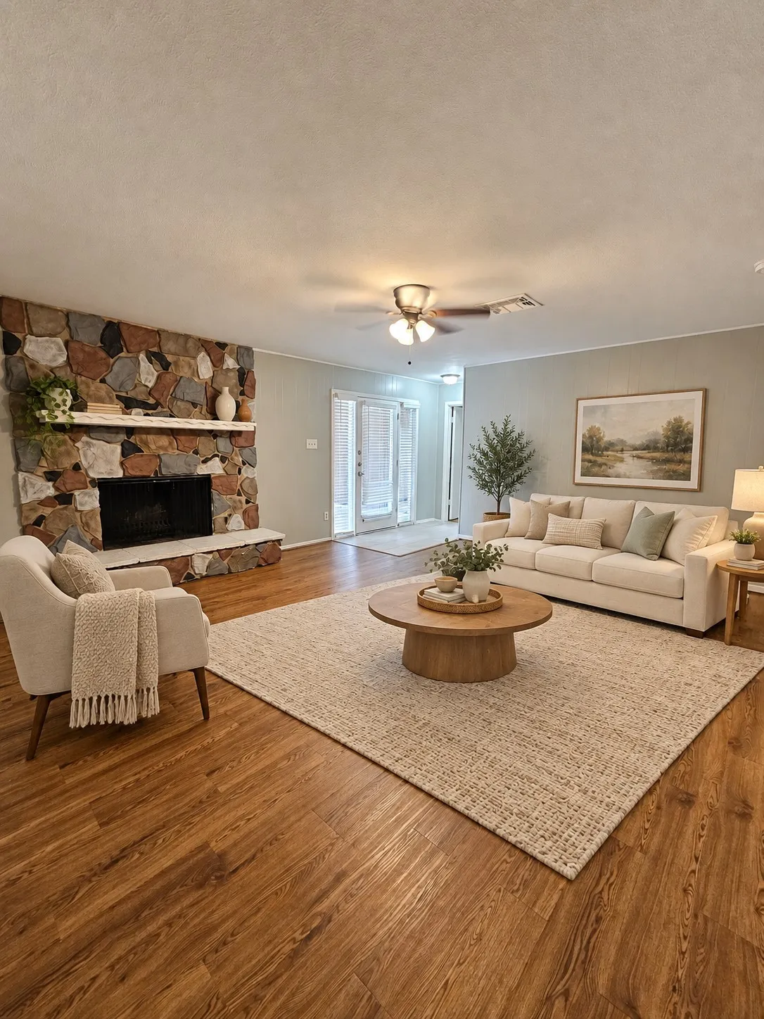Wood-finish flooring, stone-clad fireplace, and ceiling fan with integrated lighting