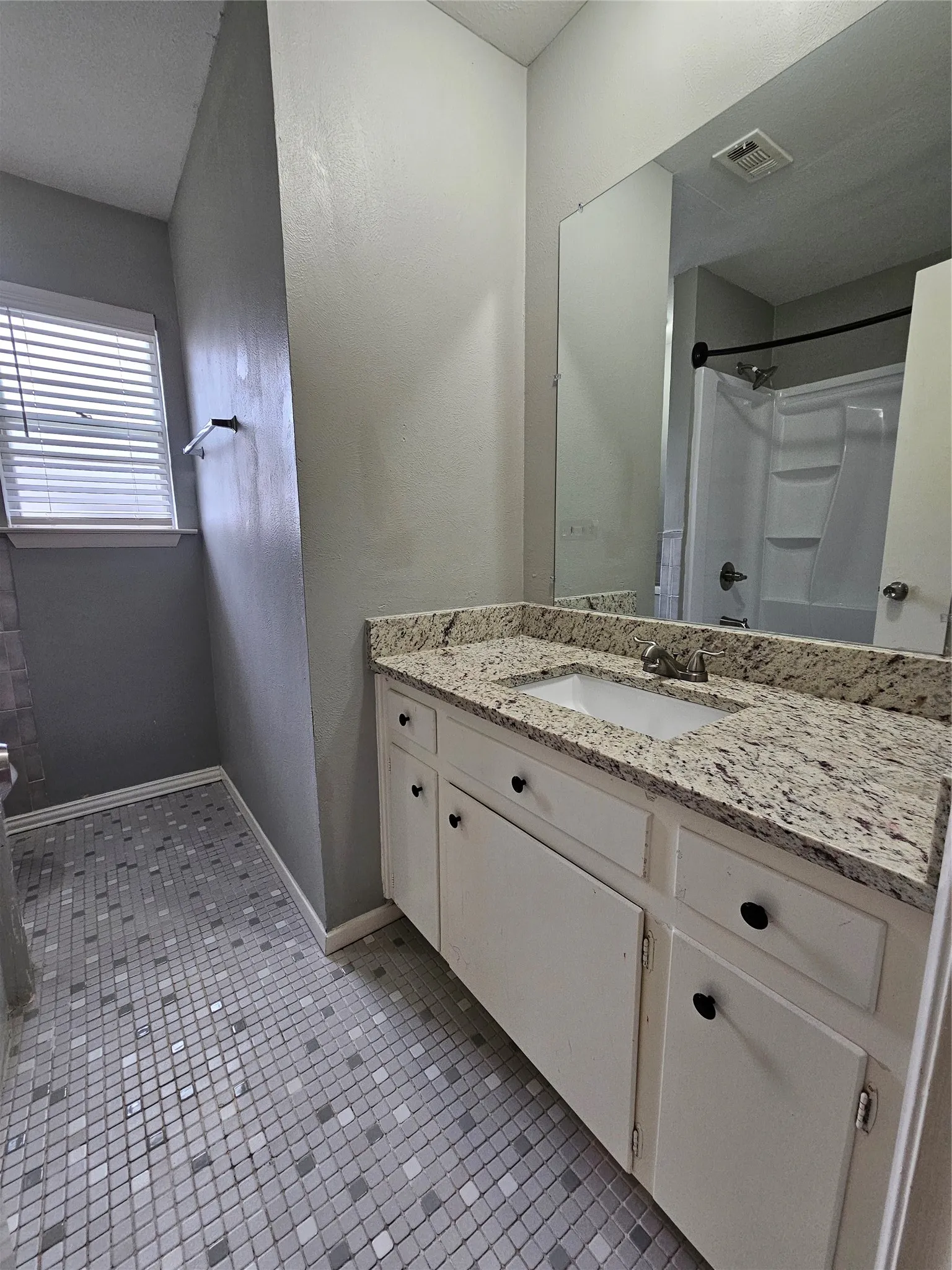 Vanity with a light-toned countertop and an integrated sink, white cabinetry with black hardware, and mosaic tile flooring