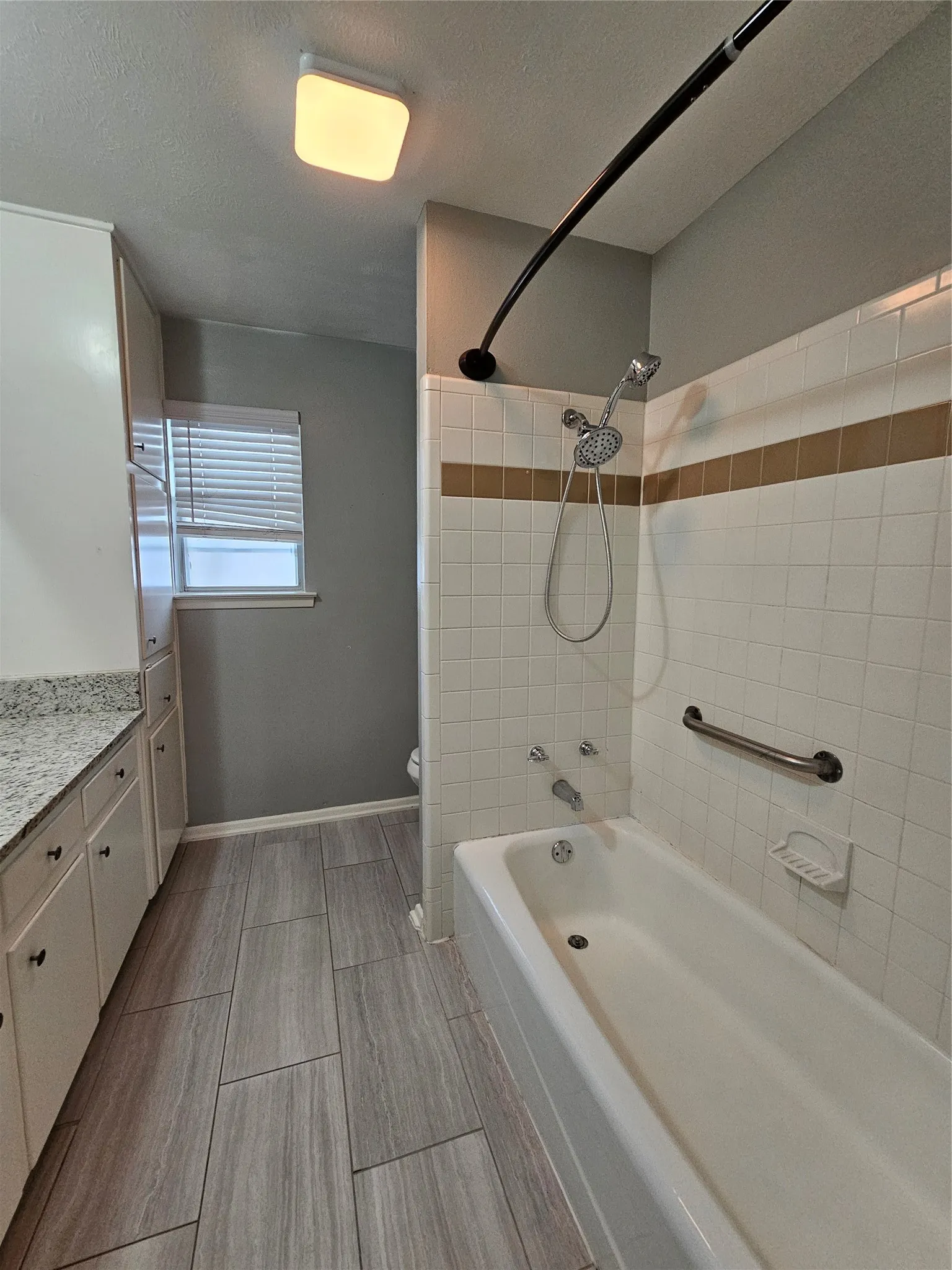 Bathtub with white subway tile surround, integrated grab bar, and shower head