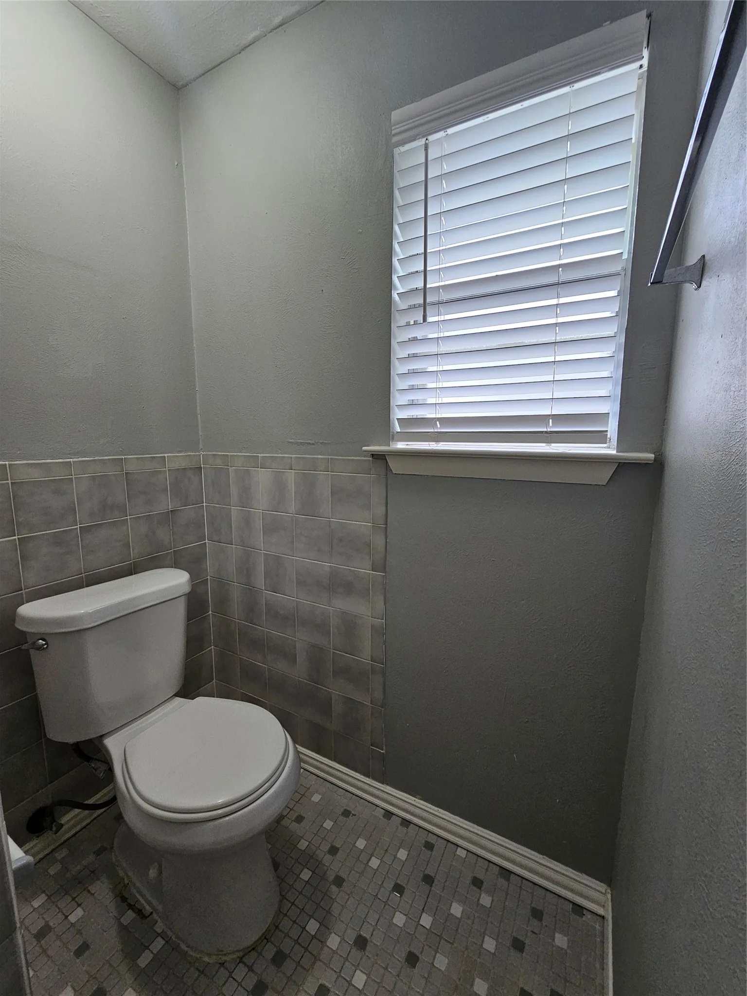 White toilet with chrome flush lever, mosaic tile flooring, and half-height wall tiling