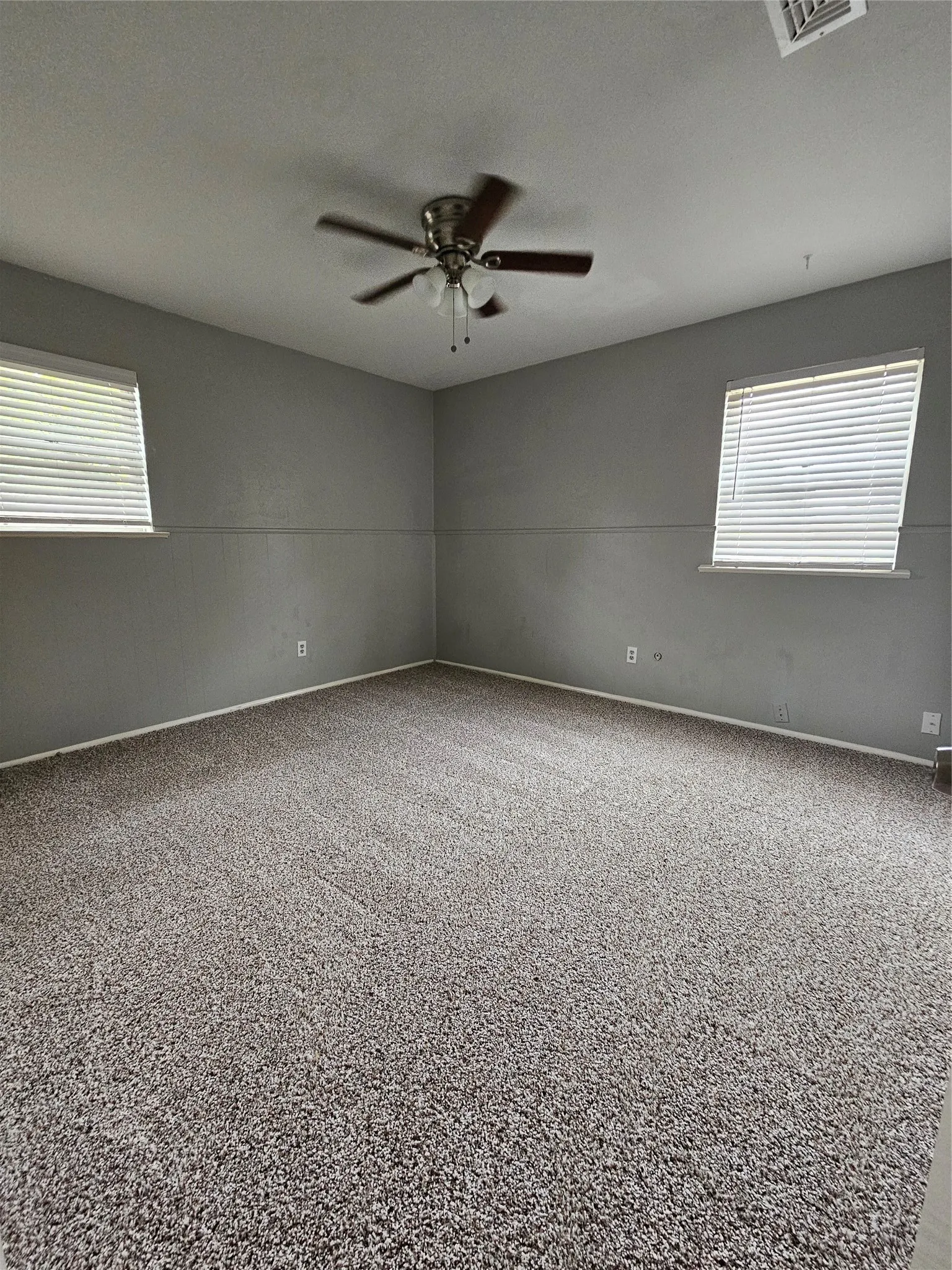 Carpeted room featuring a ceiling fan with integrated lighting and two windows with blinds