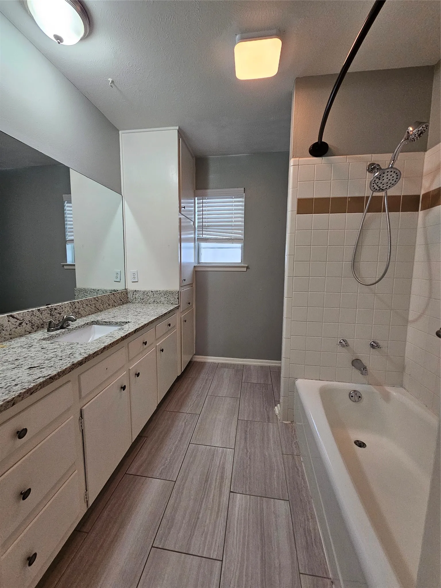 Double vanity with speckled countertop, wood-finish flooring, built-in cabinetry, tiled shower and tub combination