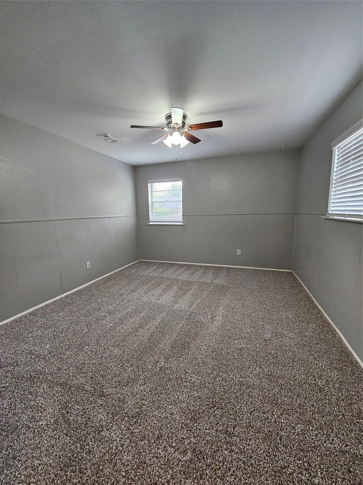 Wall-to-wall carpeting with neutral-toned walls, featuring two windows with blinds, and a ceiling fan with integrated lighting