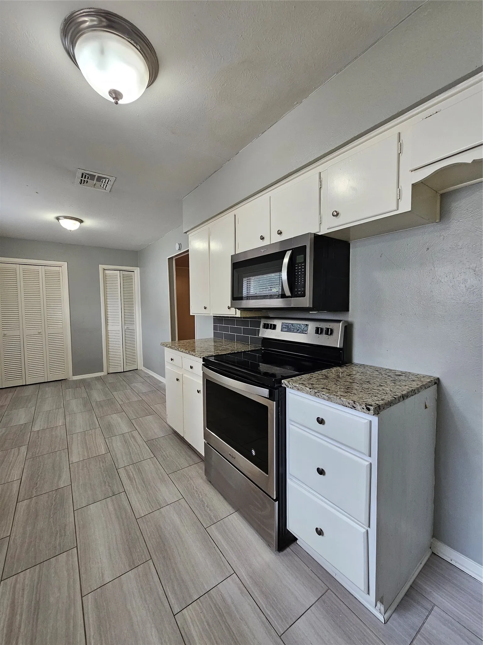 Kitchen featuring stainless steel appliances, white cabinetry, granite-finish countertops, subway tile backsplash, and large format floor tiling
