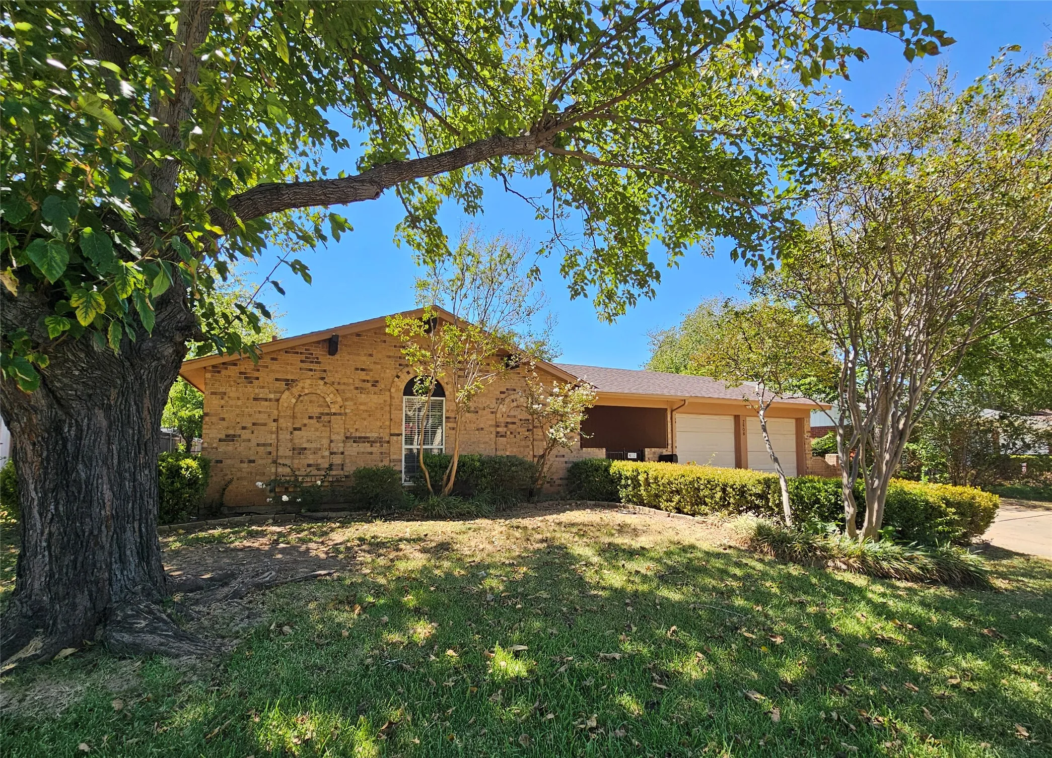 Traditional brick exterior featuring an arched window, two-car garage, and mature landscaping
