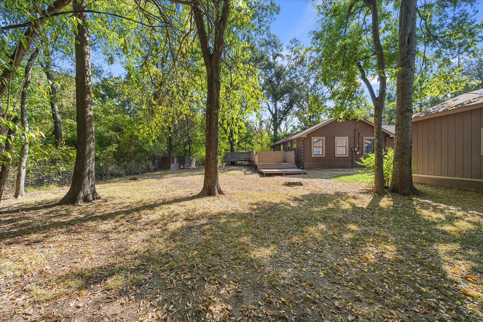 Large back yard with mature trees. This view shows the multi-level wood deck, back of the workshop and you can see the chicken coop to the left at the treeline.