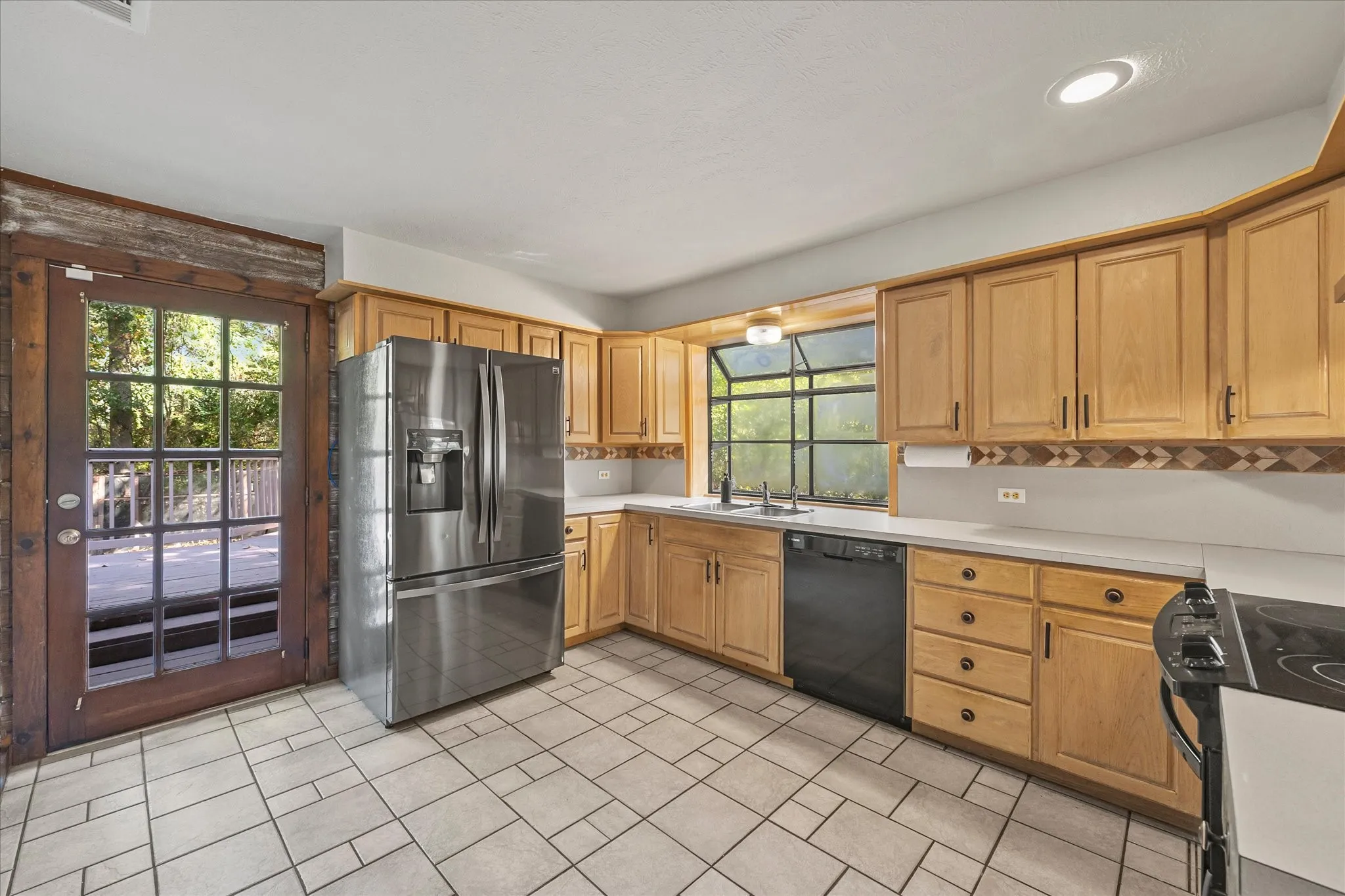 Freshly painted kitchen features tile flooring, black and stainless steel appliances, and back patio and yard access. Refrigerator tays.