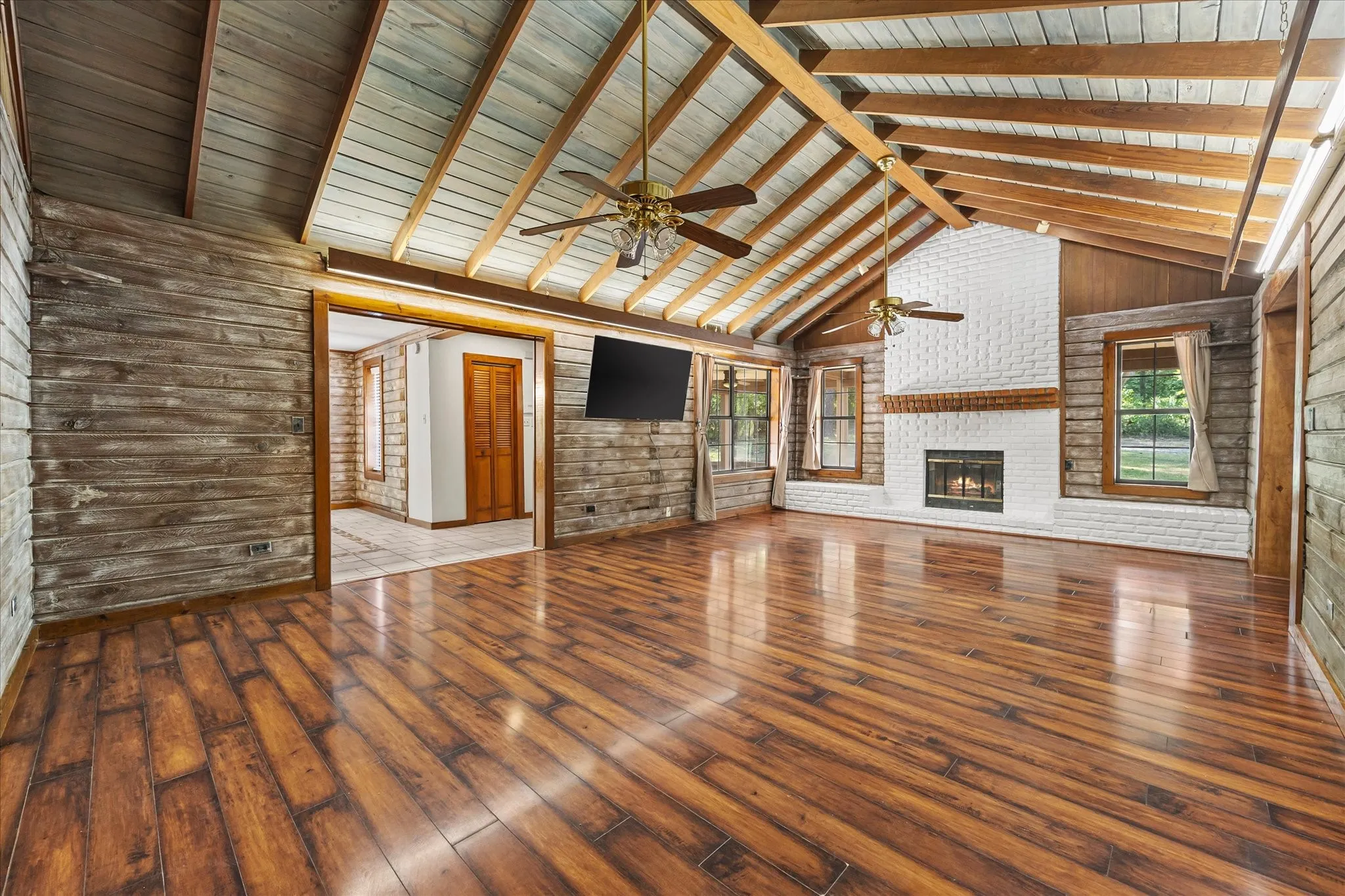 Enormous living room with vaulted and beamed ceilings, plank flooring, and wood burning fireplace.