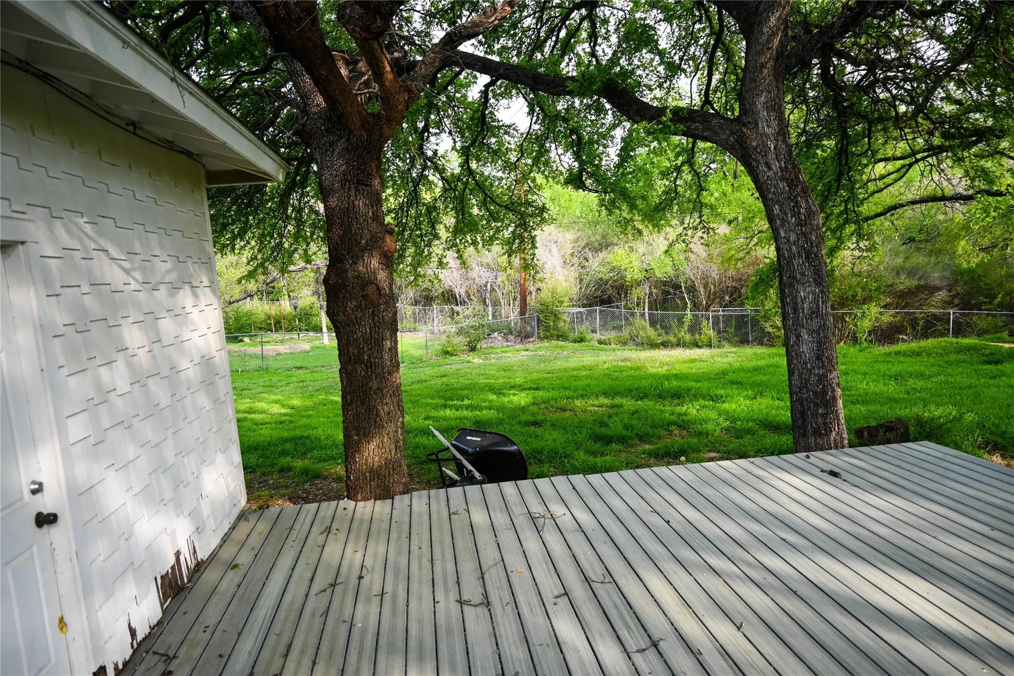 Expansive backyard featuring a manicured lawn, mature trees, and a wooden deck