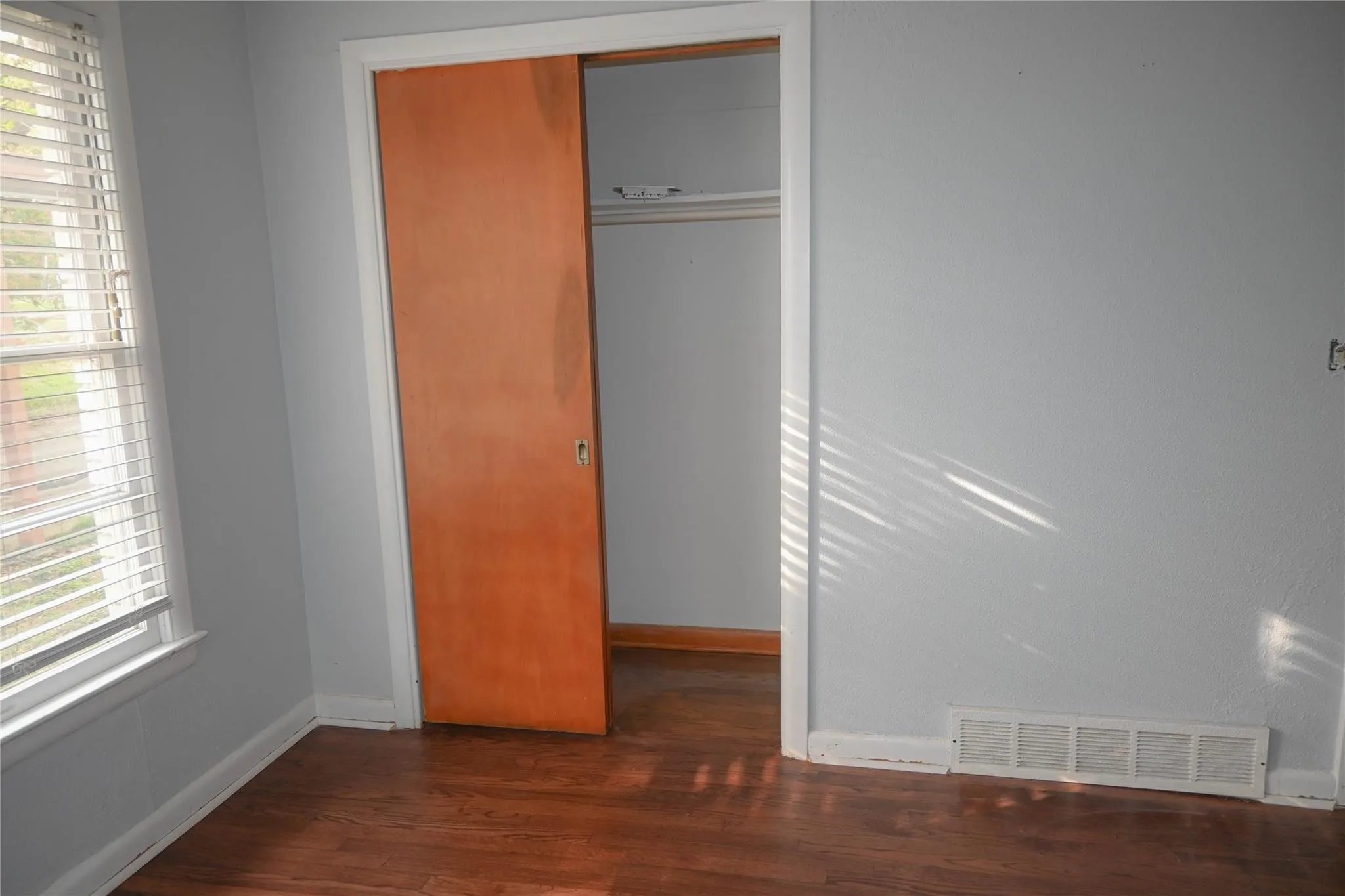 Hardwood-finish flooring, light grey wall paint, and a sliding wood-finish closet door
