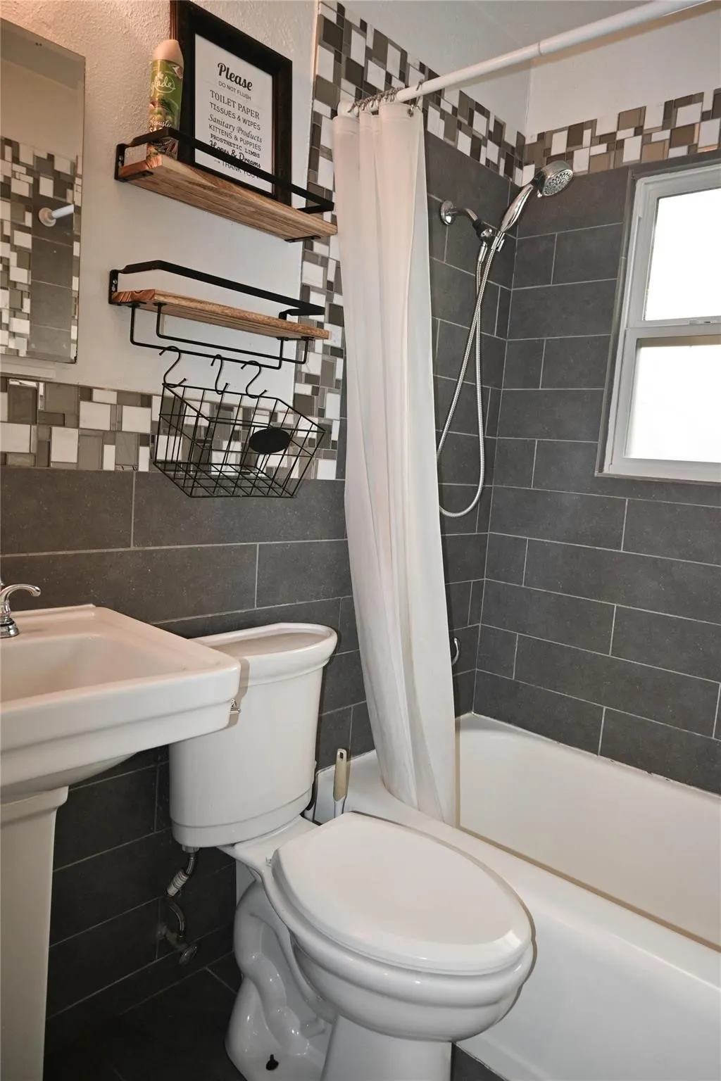 Full pedestal sink, white toilet, white bathtub, dark gray wall tiling, and a mosaic tile accent band