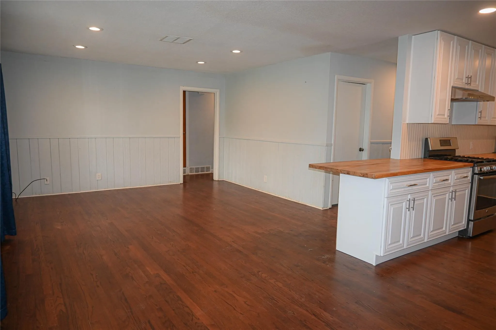 Rich wood-finish flooring throughout, recessed ceiling lighting, and white wainscoting