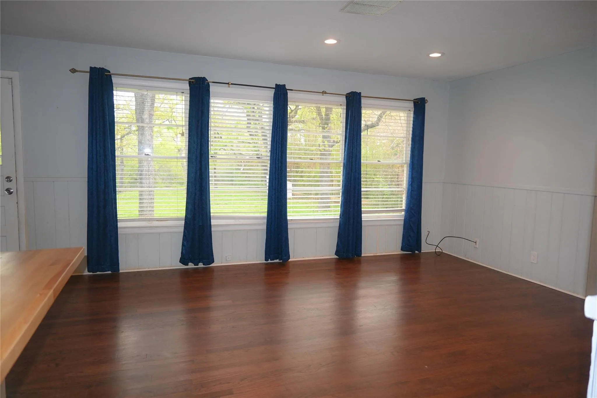 Wood-finish flooring with recessed lighting, complemented by a large window bank, and wainscoting
