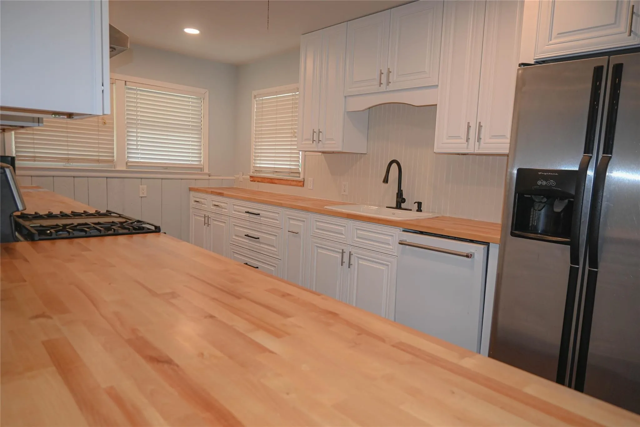 White cabinetry with black hardware, wood-finish countertops, stainless steel appliances, and beadboard backsplash