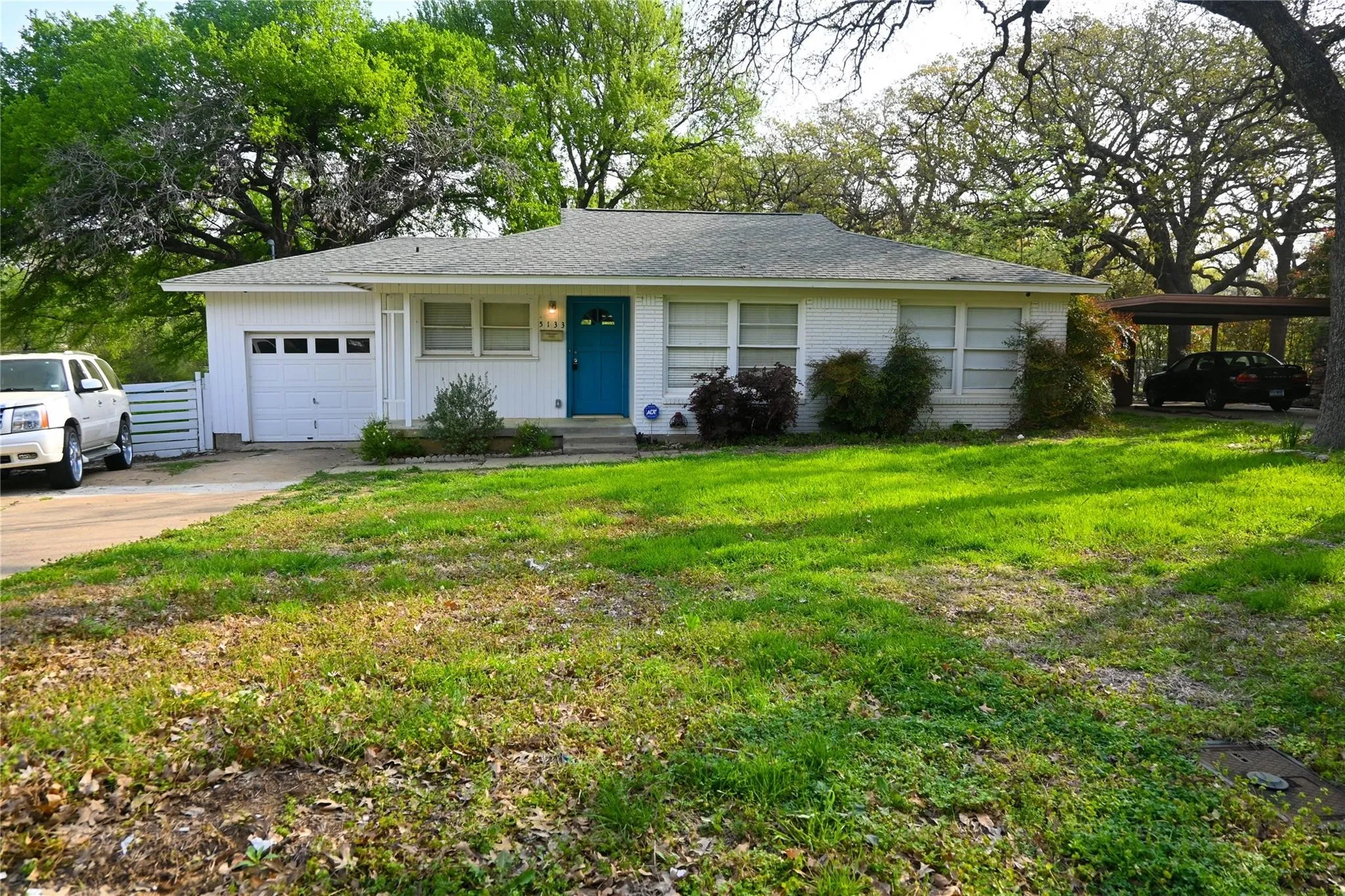 White exterior featuring a bright blue front door, attached garage, and a covered carport