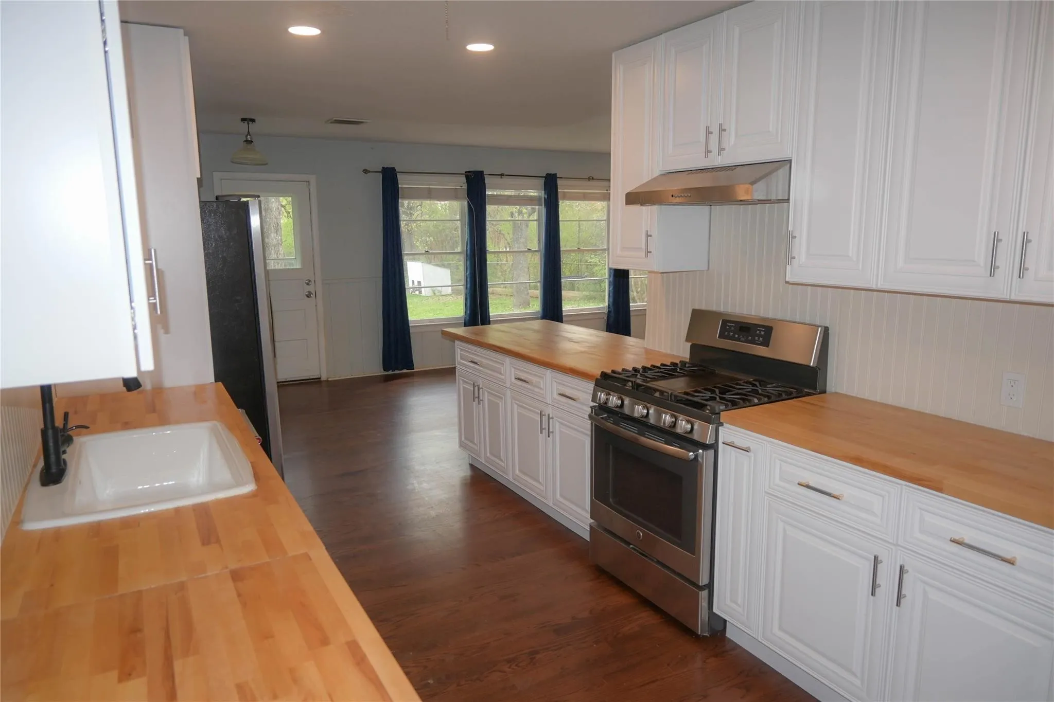 Kitchen featuring wood-finish countertops, white cabinetry, stainless steel range, and a white sink with a black faucet