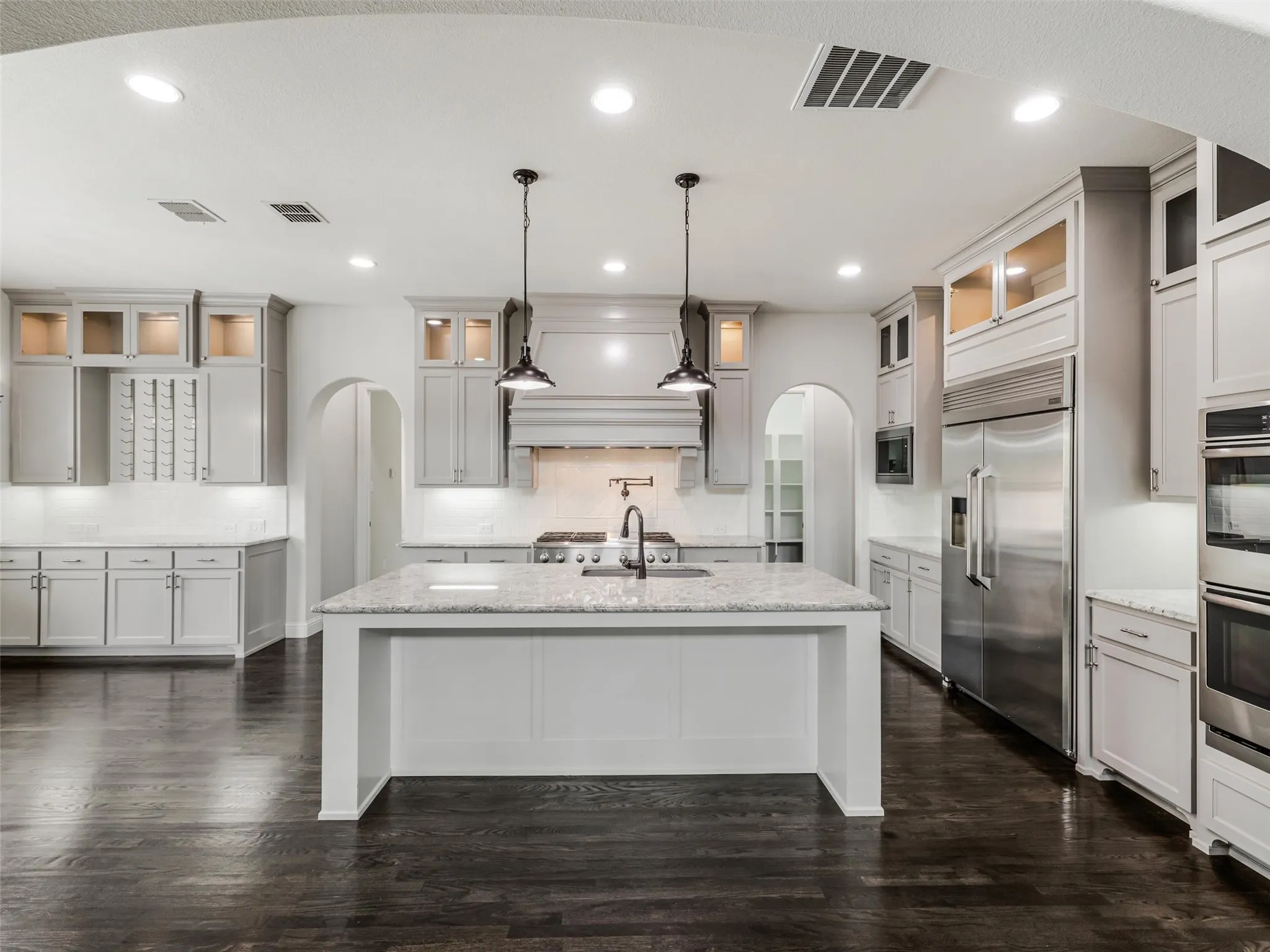 At the heart of the home is a beautifully appointed kitchen featuring custom built-in cabinetry and an impressive collection of stainless-steel appliances. A commercial-grade gas cooktop with coordinating hood provides a centerpiece for the space, complemented by a built-in refrigerator, double ovens, built-in microwave, and a new dishwasher installed in 2025. The large center island offers breakfast bar seating and generous workspace, making the kitchen equally suited for everyday meals and entertaining.