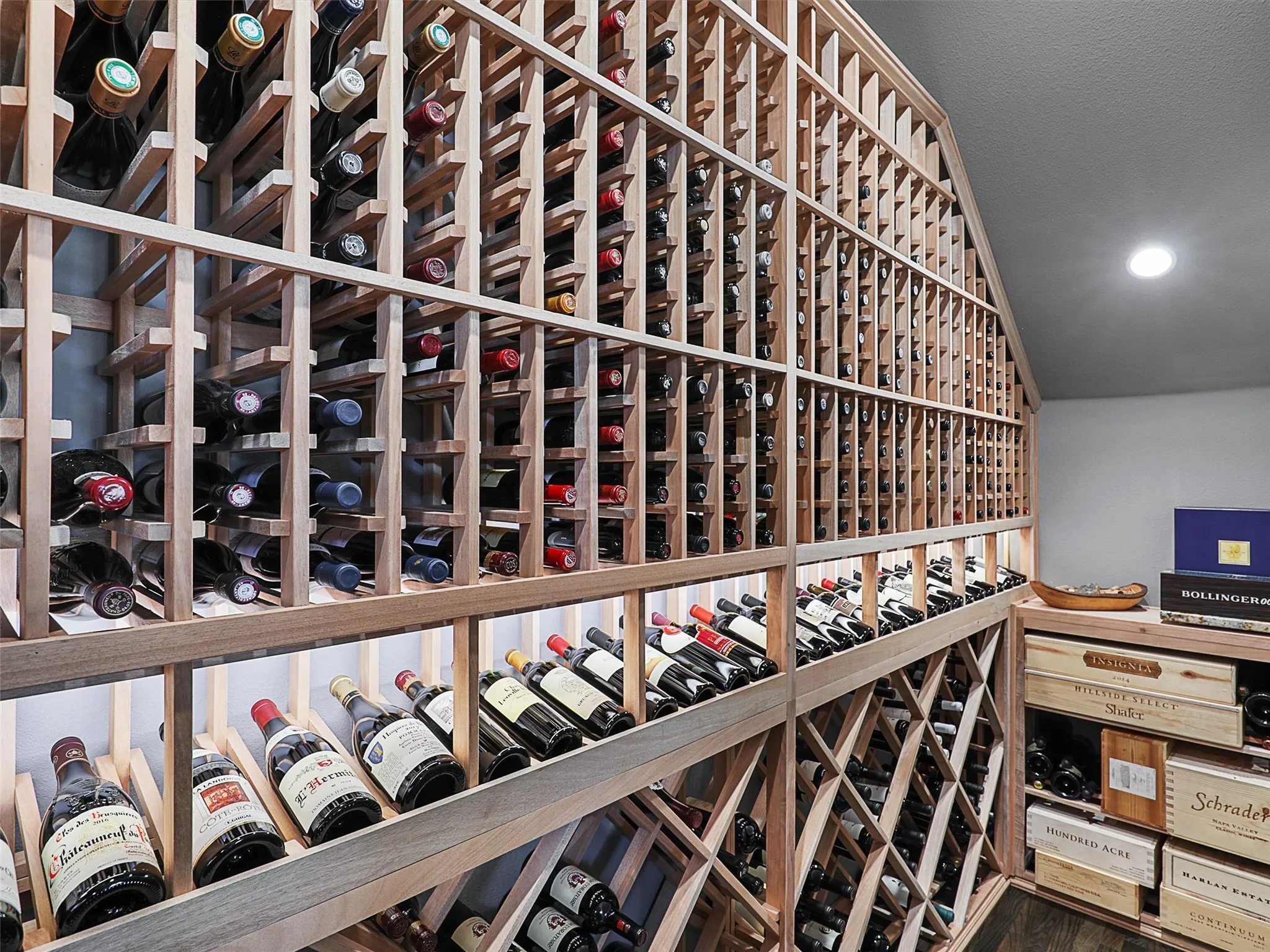 One of the home's most distinctive features is its custom wine cellar, completed in 2022 and designed for the serious wine enthusiast. The cellar features a CellarPro 4000S split-system cooling unit engineered to regulate both temperature and humidity. Hard foam insulation within the walls and ceiling, along with moisture-resistant drywall, helps create a controlled environment for the collection. A custom iron entry door with UV-protective glass introduces the space, while custom solid mahogany racking accommodates standard 750ml bottles, larger champagne-style bottles, large-format bottles, and wood cases. Multiple lighting zones with dimmers create an elegant atmosphere, while storage capacity for approximately 800 bottles transforms the cellar into both a functional collection space and a striking architectural feature.
