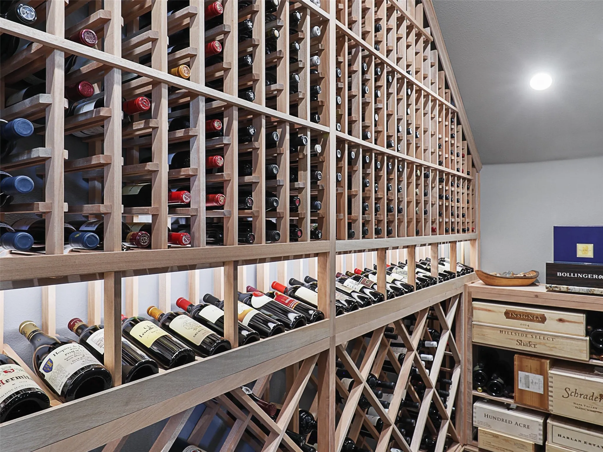 One of the home's most distinctive features is its custom wine cellar, completed in 2022 and designed for the serious wine enthusiast. The cellar features a CellarPro 4000S split-system cooling unit engineered to regulate both temperature and humidity. Hard foam insulation within the walls and ceiling, along with moisture-resistant drywall, helps create a controlled environment for the collection. A custom iron entry door with UV-protective glass introduces the space, while custom solid mahogany racking accommodates standard 750ml bottles, larger champagne-style bottles, large-format bottles, and wood cases. Multiple lighting zones with dimmers create an elegant atmosphere, while storage capacity for approximately 800 bottles transforms the cellar into both a functional collection space and a striking architectural feature.