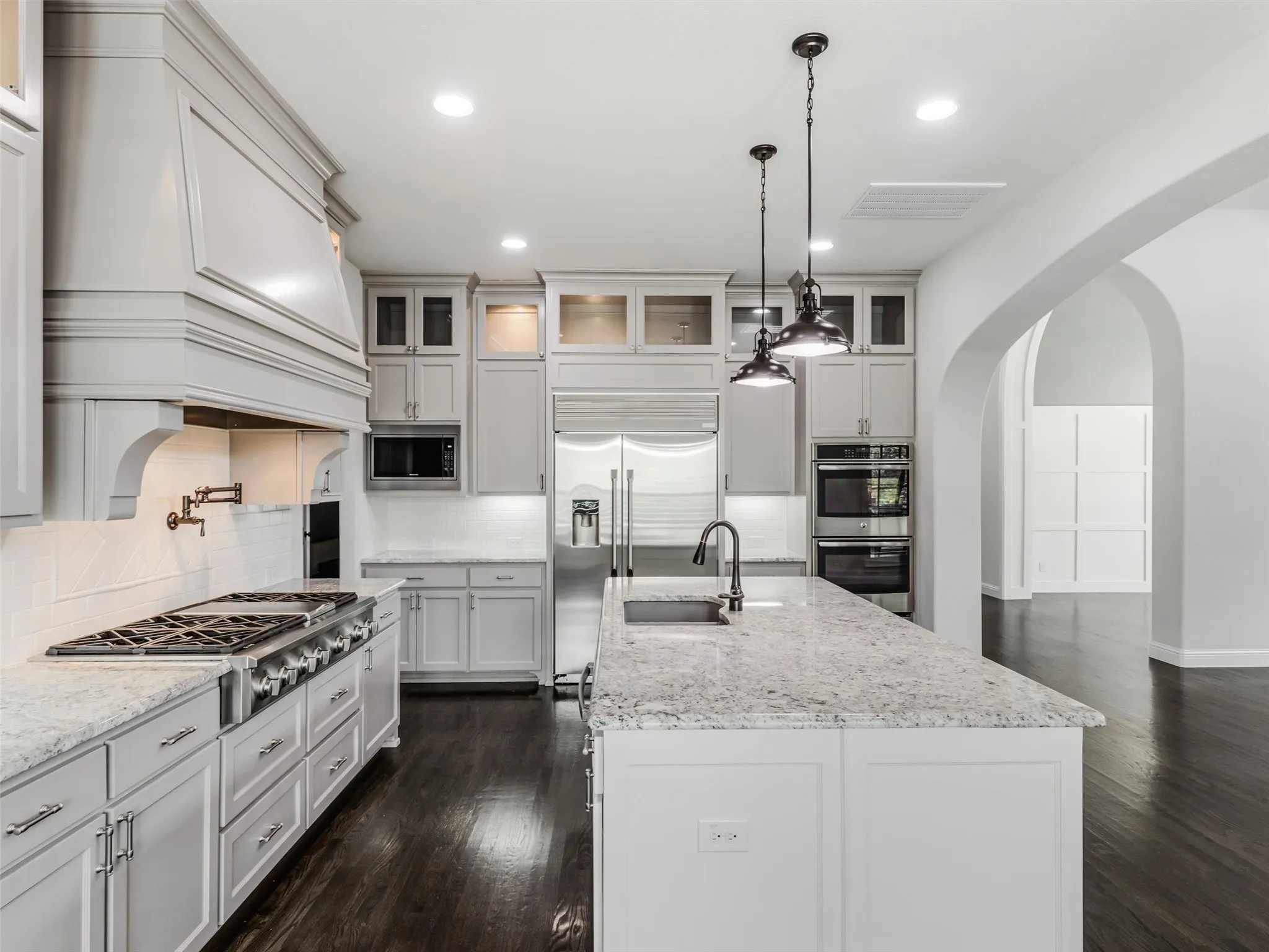 At the heart of the home is a beautifully appointed kitchen featuring custom built-in cabinetry and an impressive collection of stainless-steel appliances. A commercial-grade gas cooktop with coordinating hood provides a centerpiece for the space, complemented by a built-in refrigerator, double ovens, built-in microwave, and a new dishwasher installed in 2025. The large center island offers breakfast bar seating and generous workspace, making the kitchen equally suited for everyday meals and entertaining.