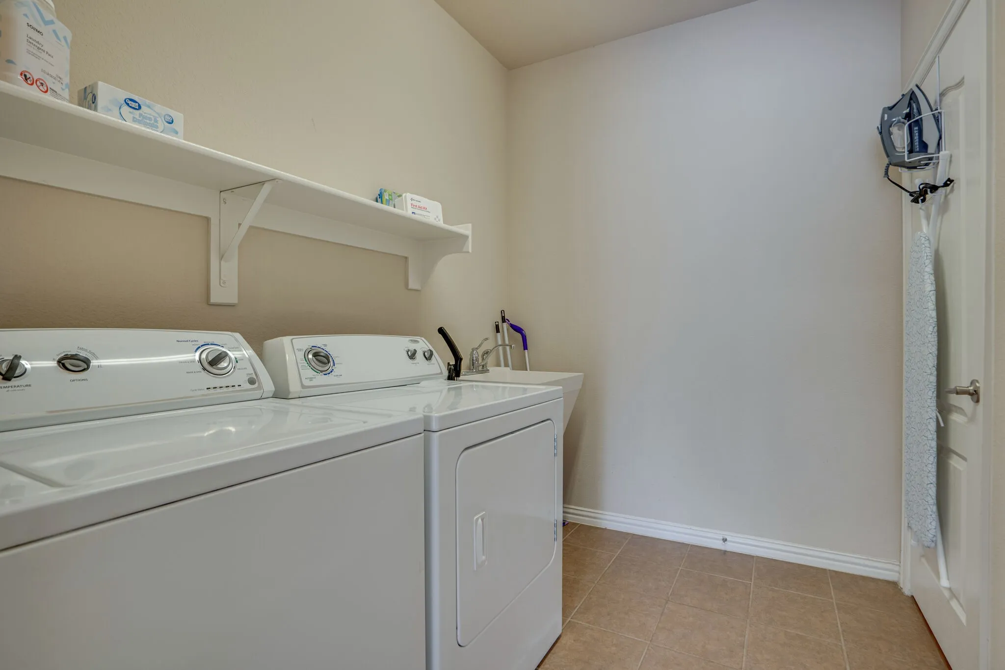 Laundry area featuring a utility sink, white shelving, and tiled flooring