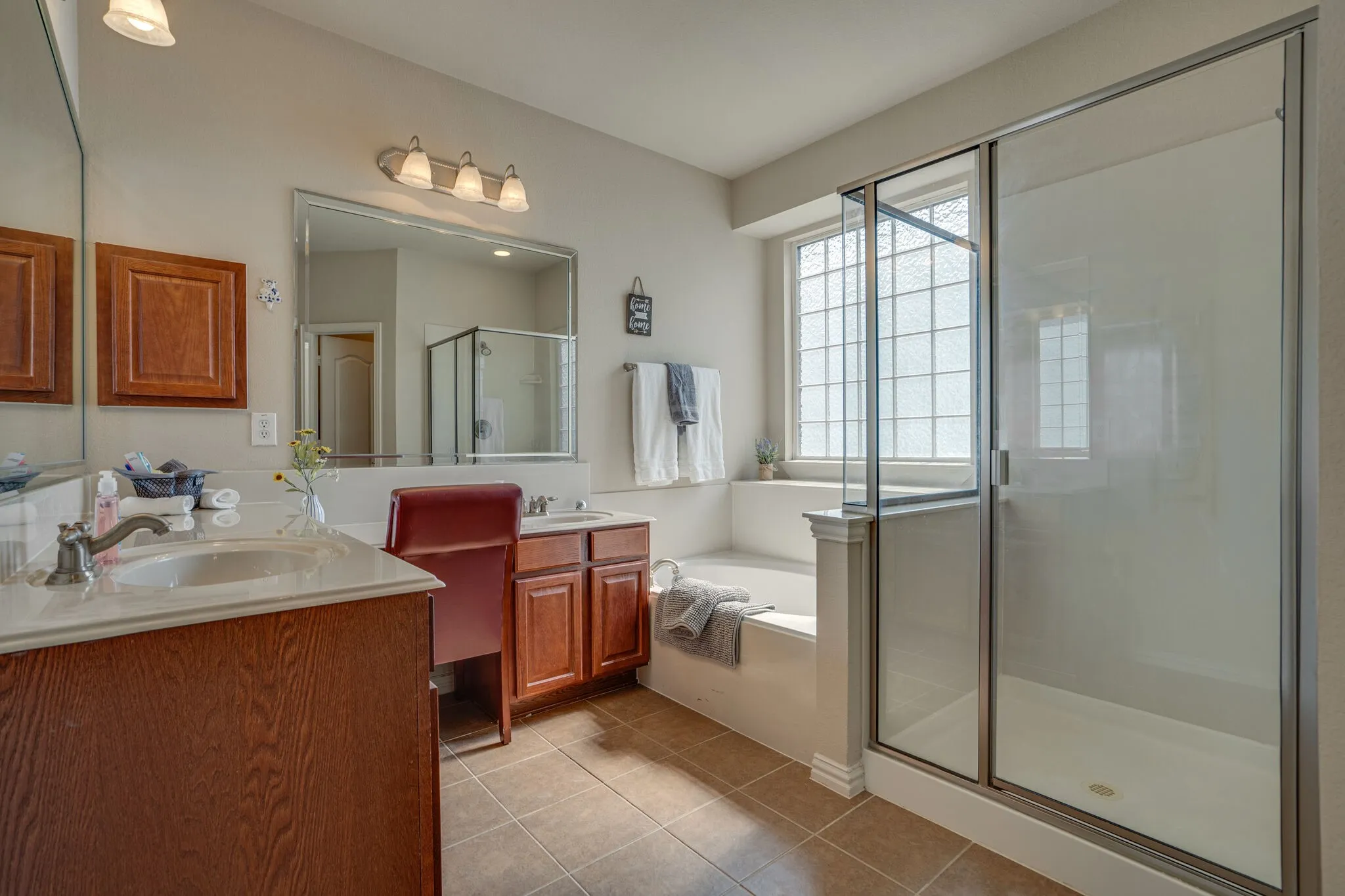 Dual vanities with integrated sinks, a built-in soaking tub, and a separate glass-enclosed shower